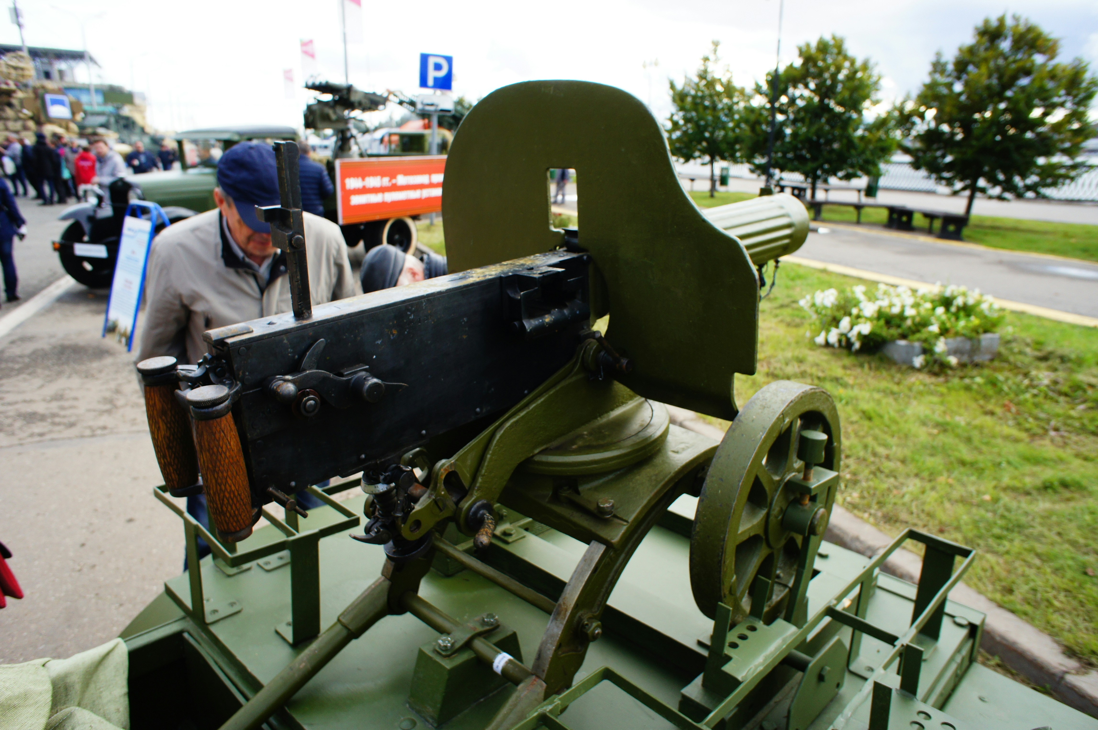 A vintage green machine gun on a wheeled mount at an outdoor exhibition