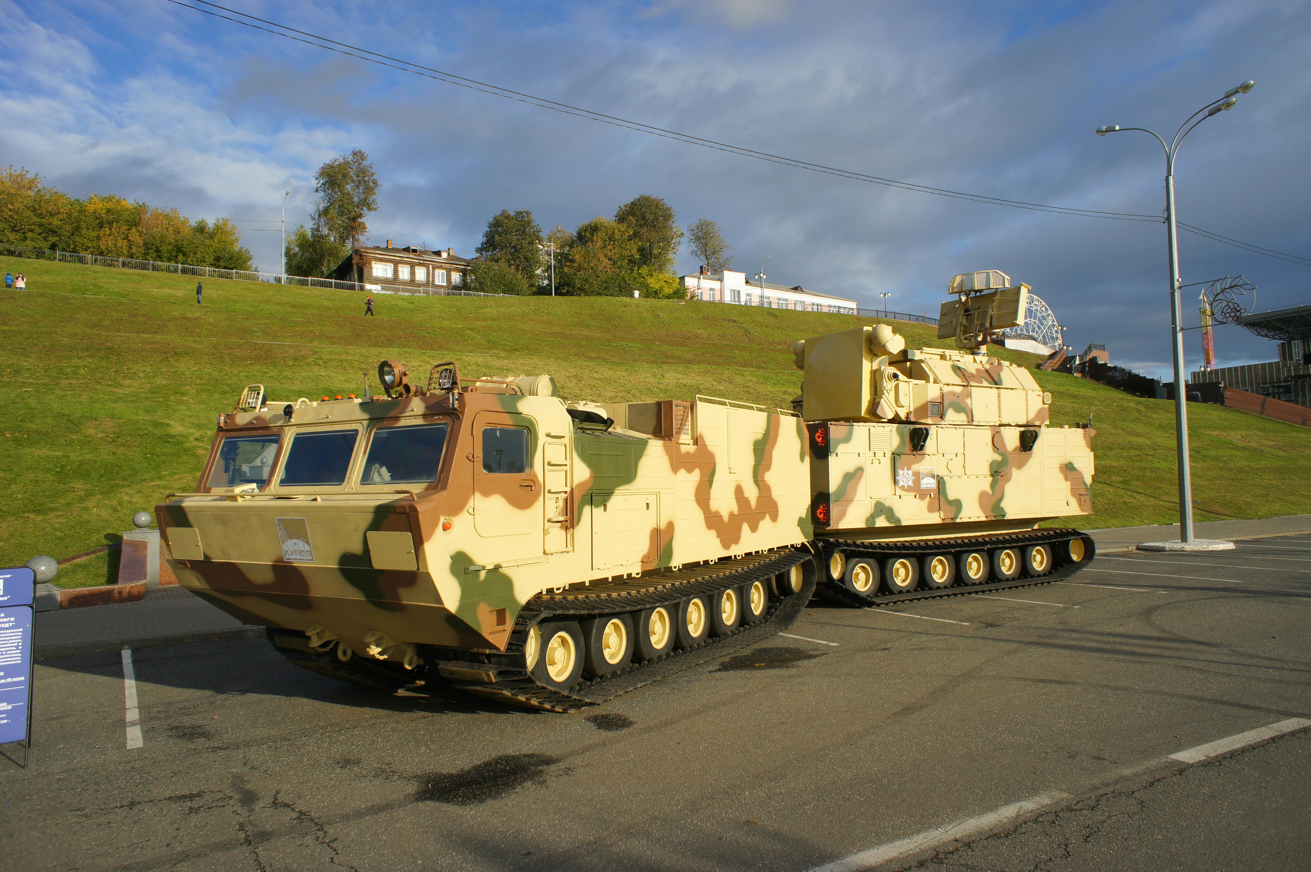 A camouflaged military vehicle with a radar system parked on an asphalt lot