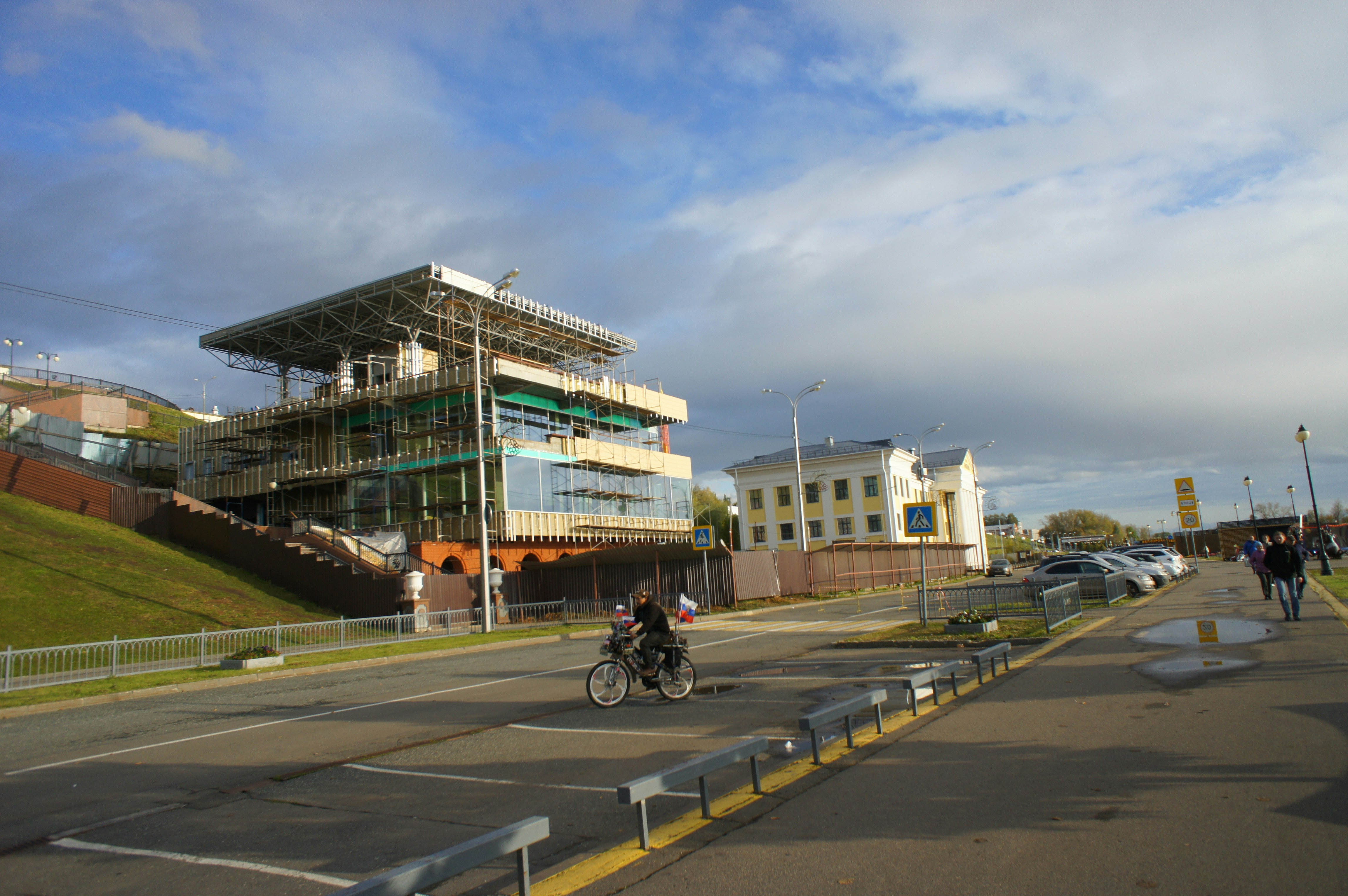 A person cycling past a building under construction near a yellow historic structure