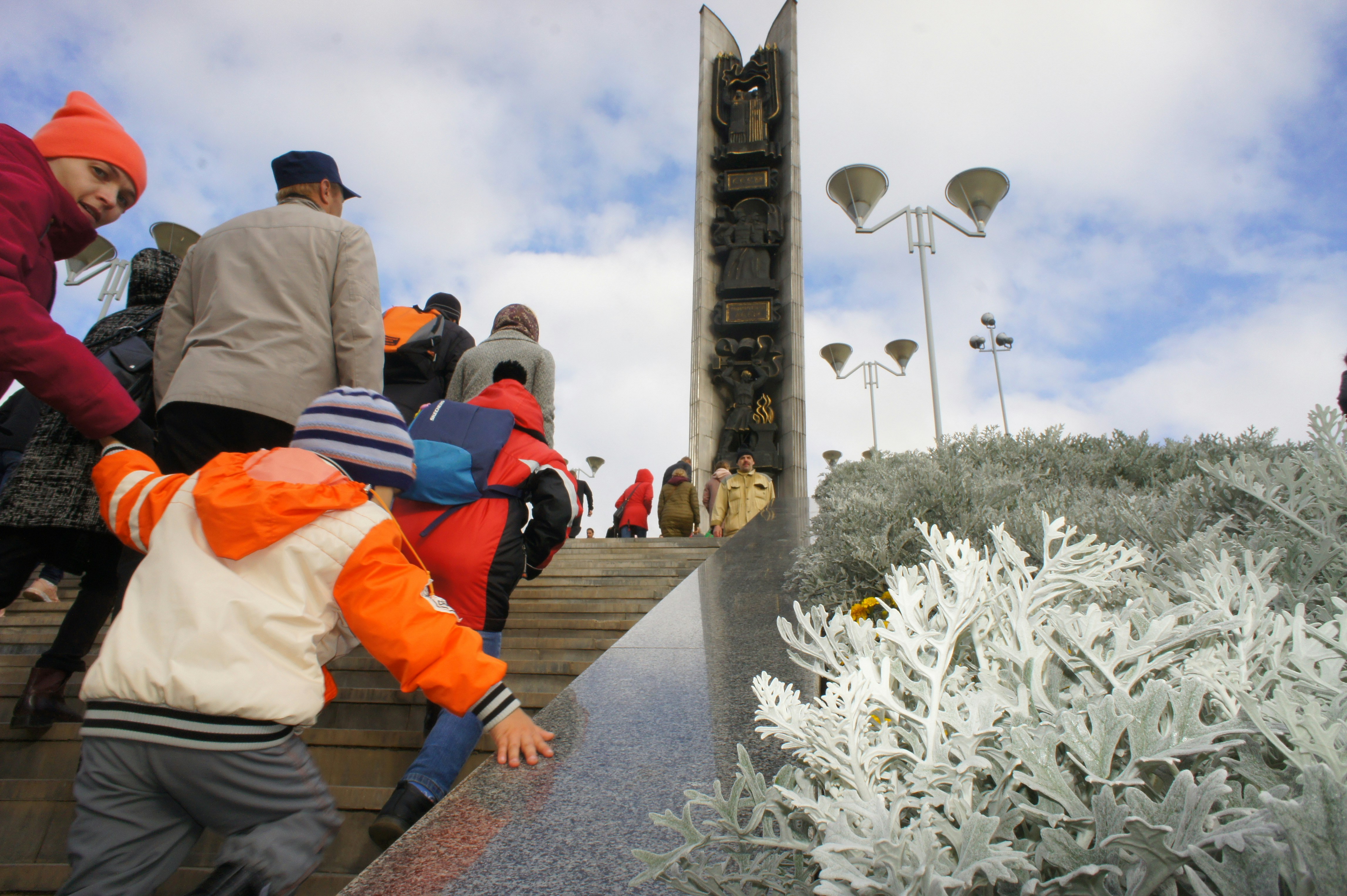 People walking up stone stairs toward a tall monument under a cloudy sky