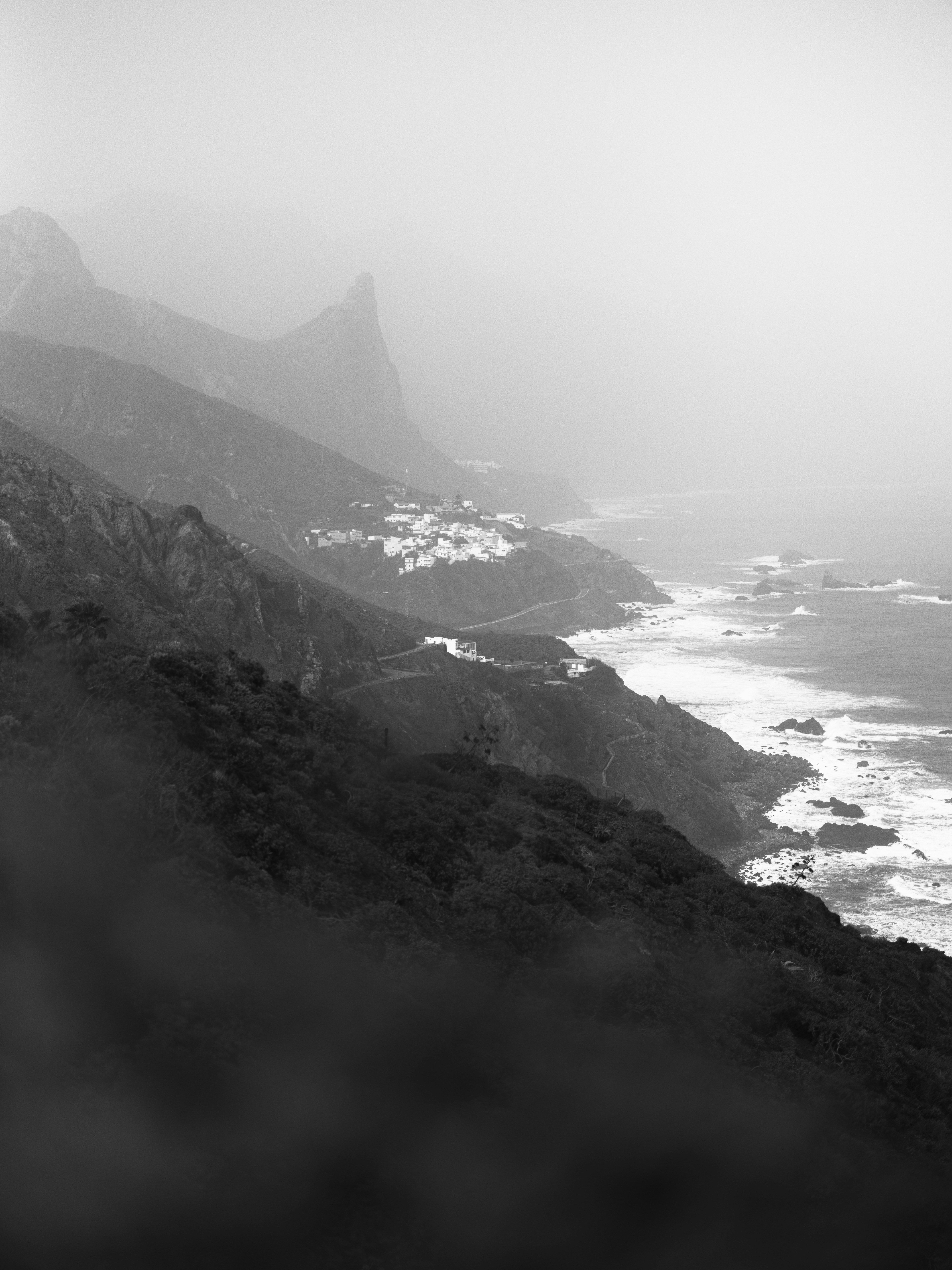 A black and white view of a coastal village nestled on misty mountains