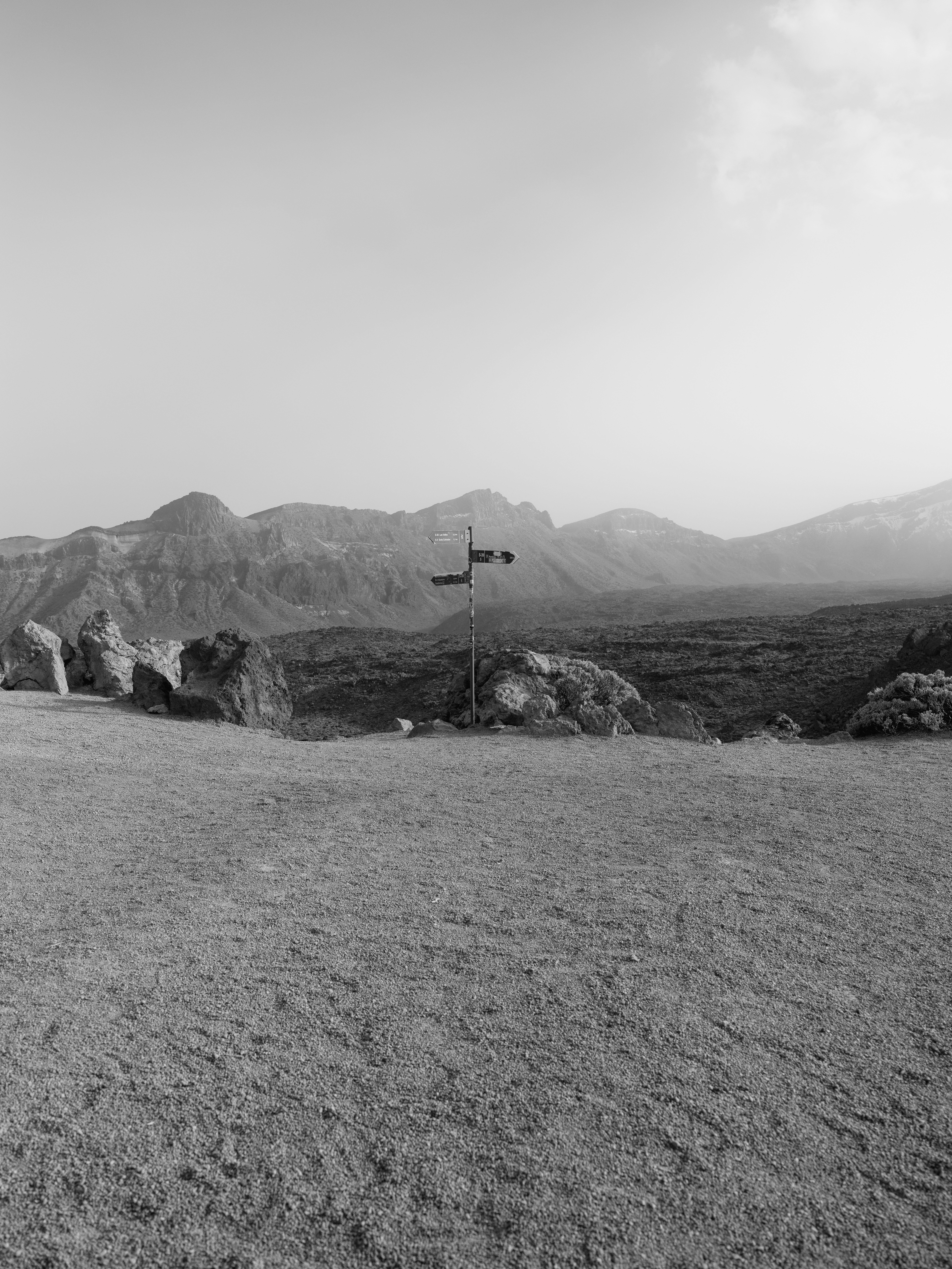 A black and white view of a trail signpost in a volcanic landscape