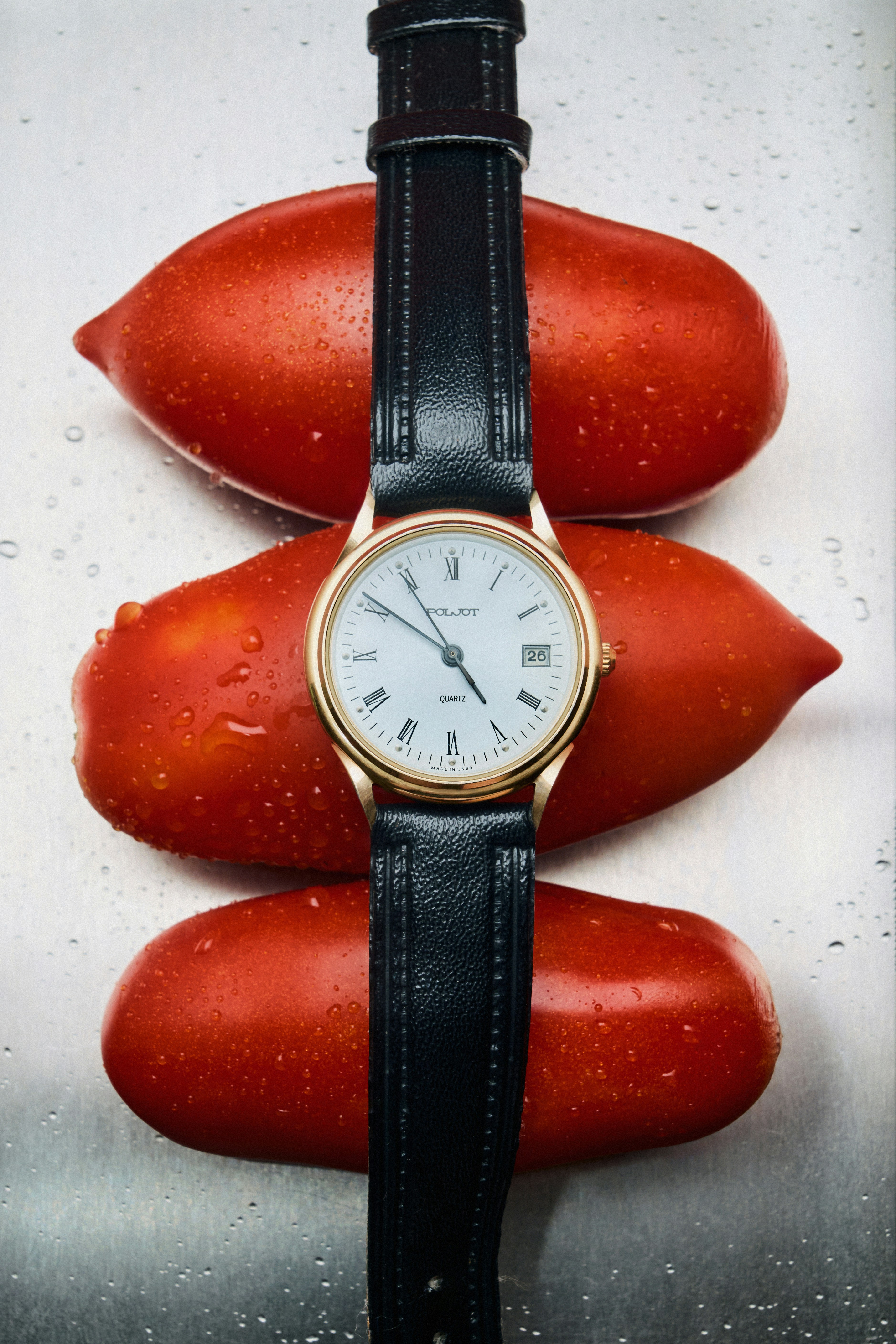 A Poljot wristwatch with a black leather strap resting on three red tomatoes