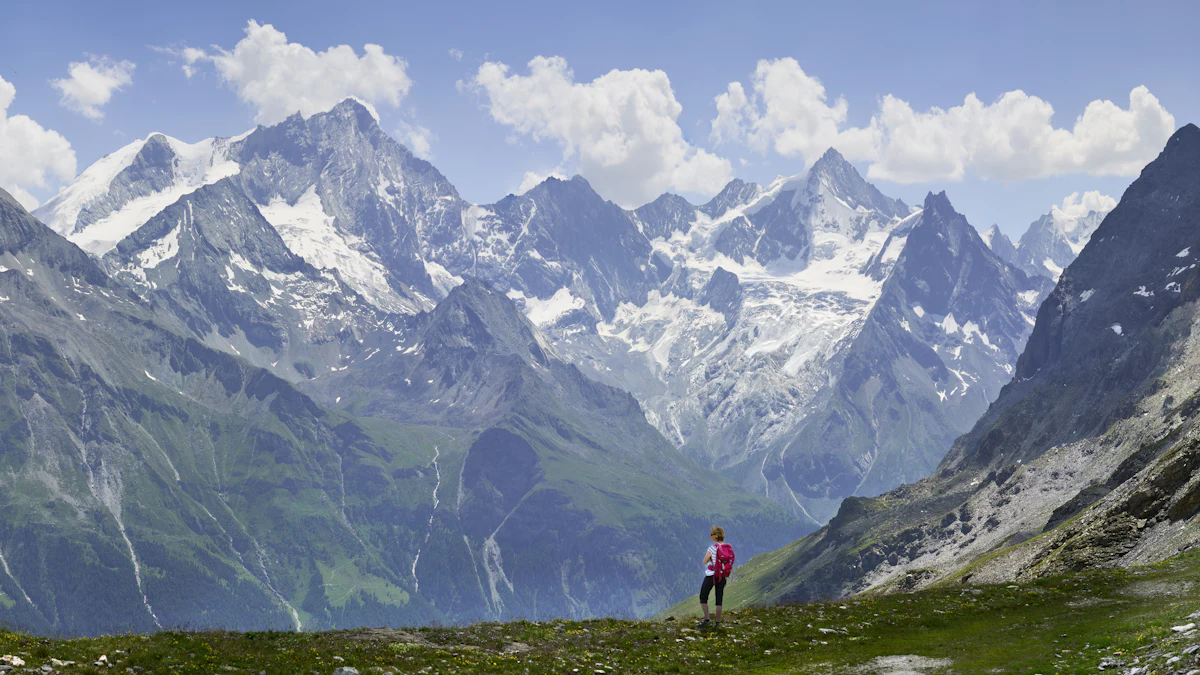 A hiker on a grassy ridge above Zinal facing the snowy peaks at the head of the Val d'Anniviers