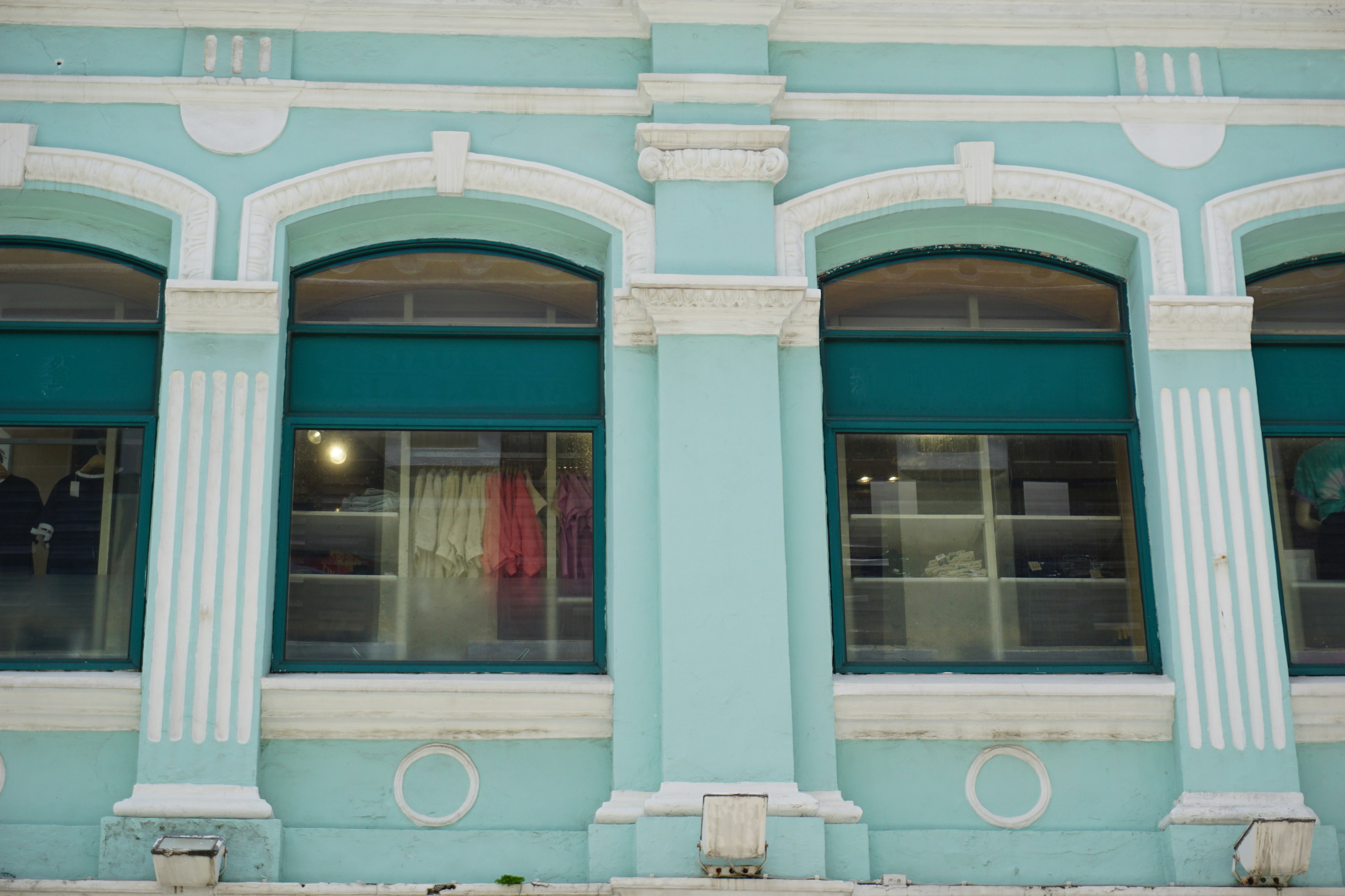 A light blue building facade with arched windows displaying clothing on shelves