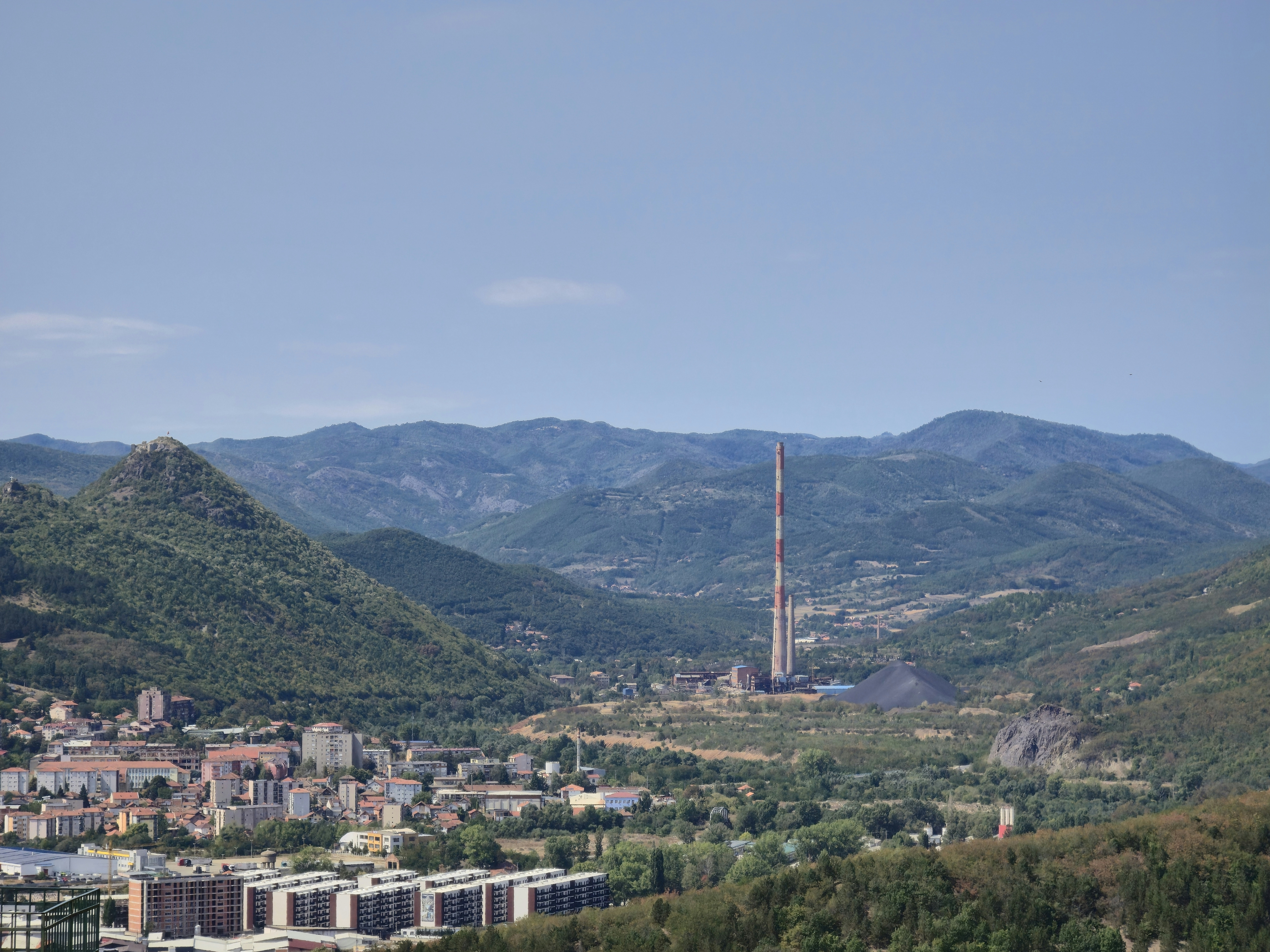 Une ville nichée dans une vallée avec une haute cheminée industrielle et des montagnes