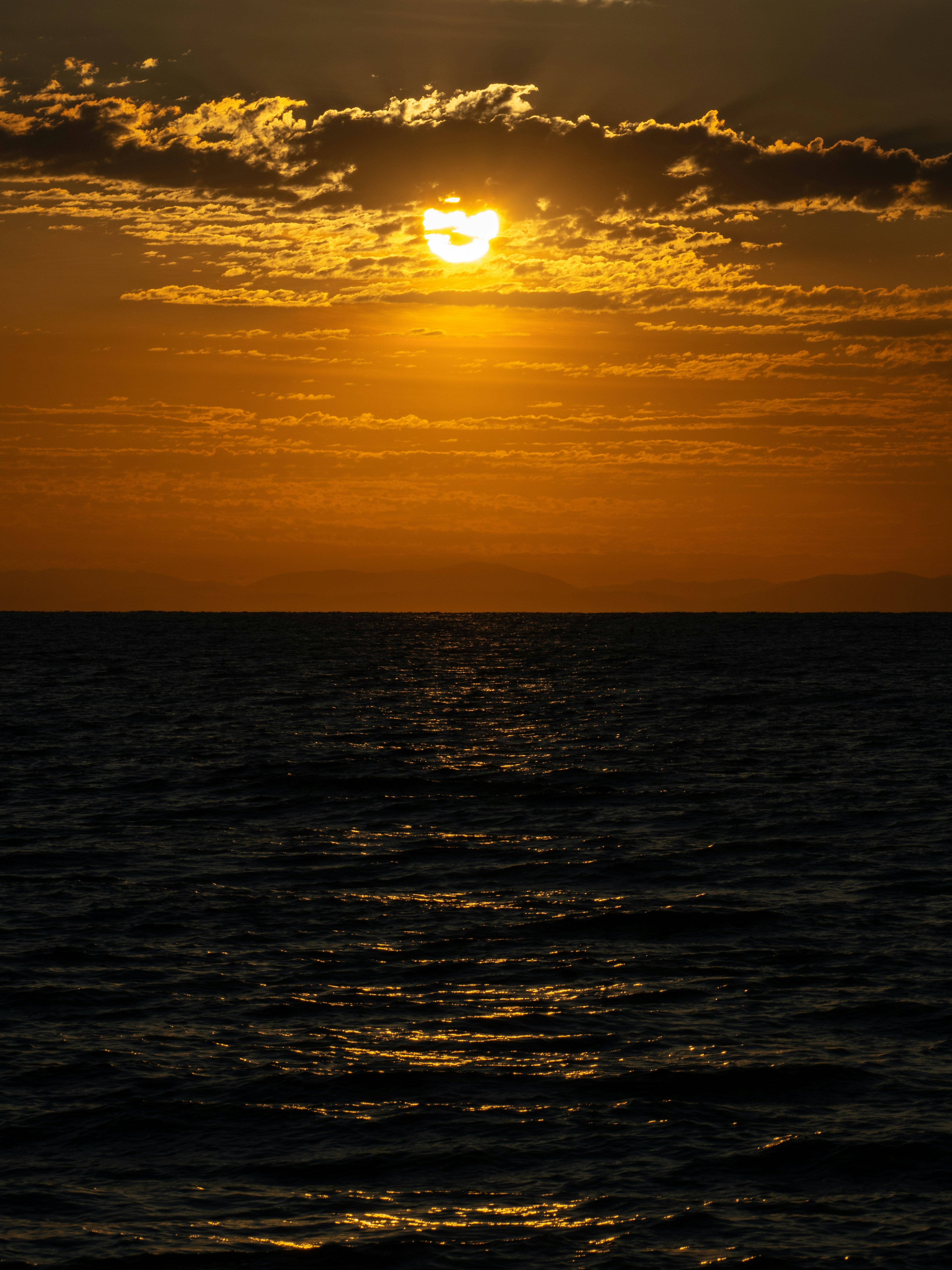 Low sun glowing through clouds above a dark sea with rippling water