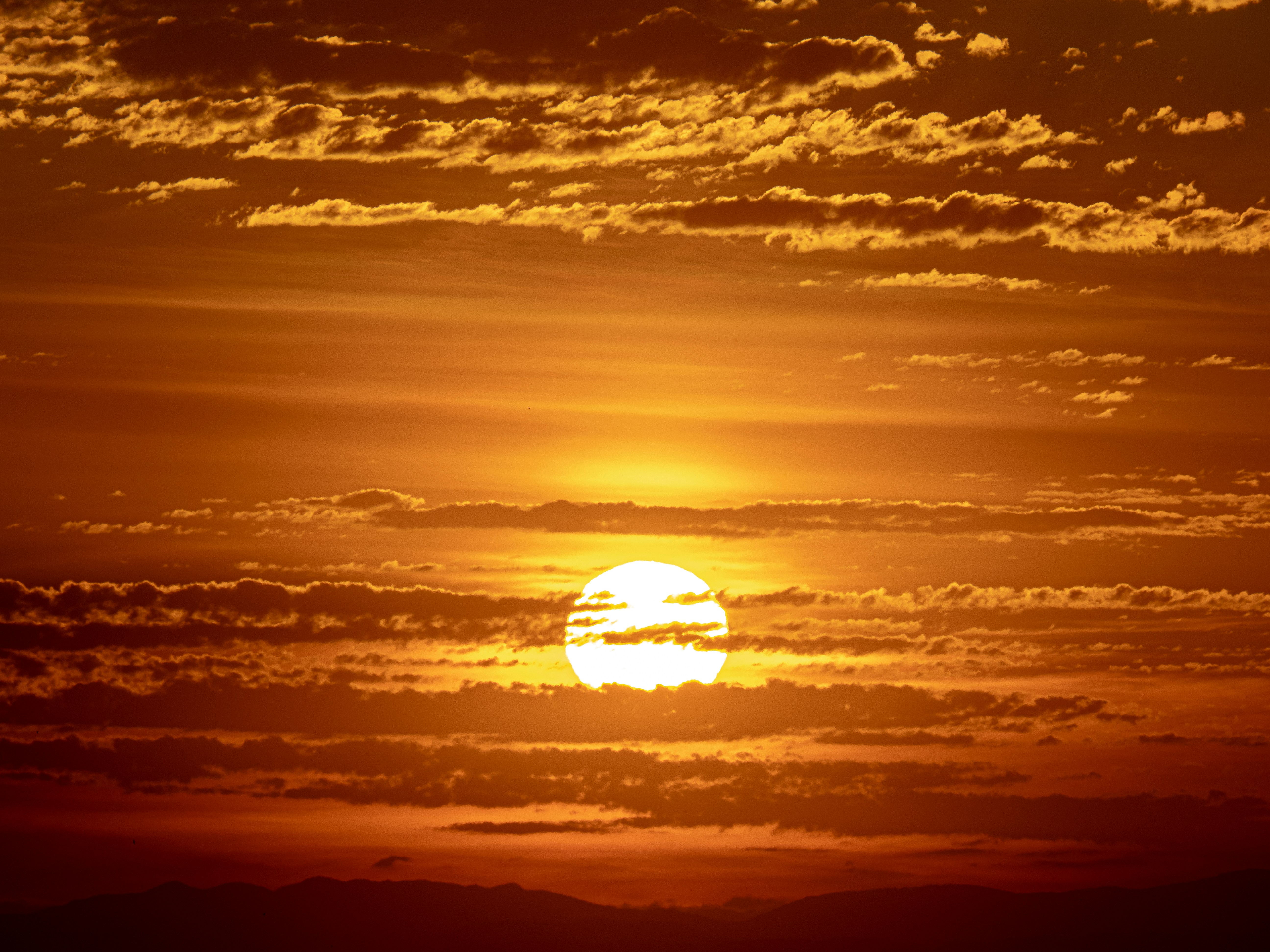 The low sun glowing behind thin horizontal clouds in a warm orange sky