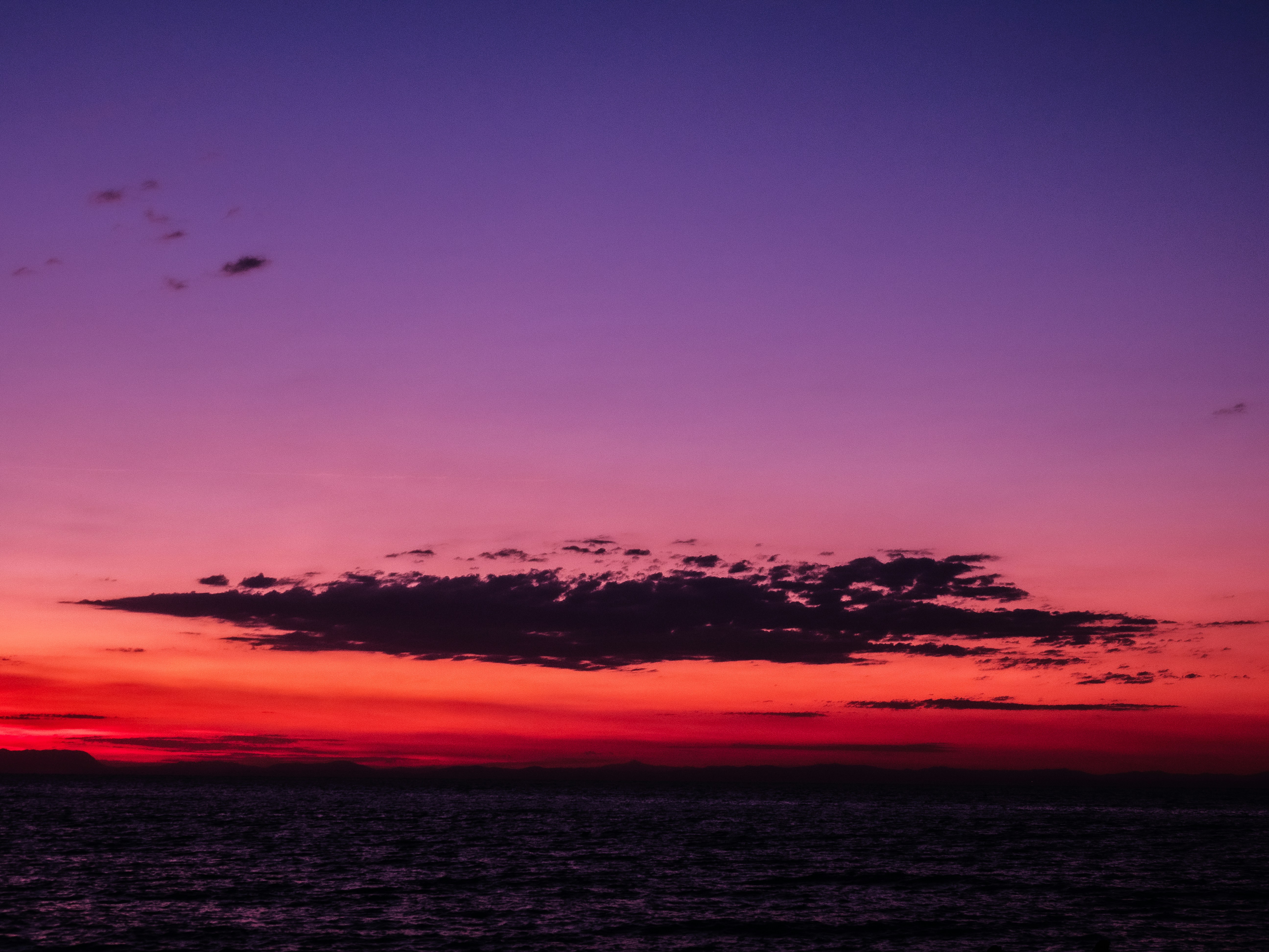 A vibrant purple and red sky above a dark ocean horizon