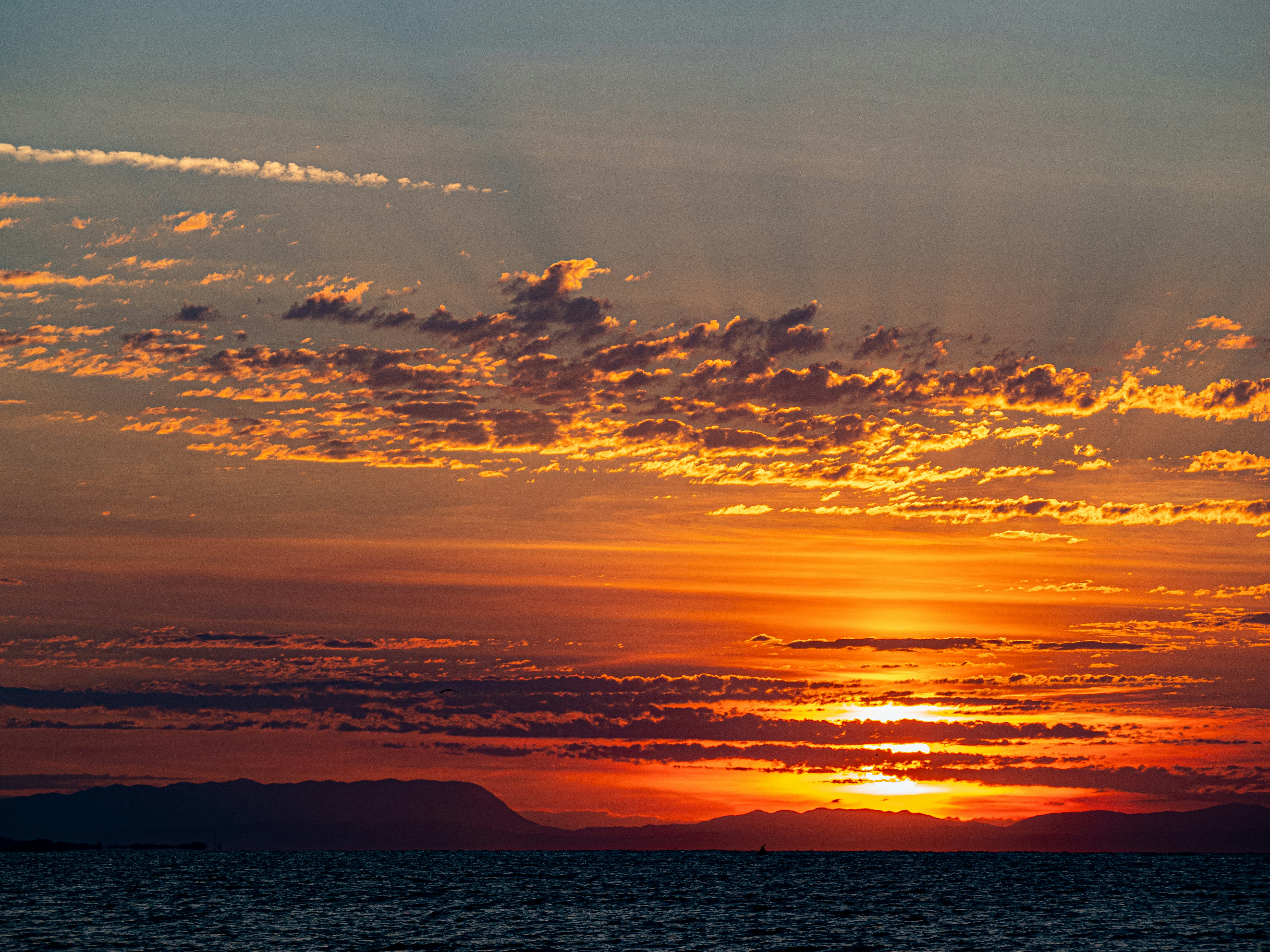 Low sun casting golden light over clouds above a dark mountain silhouette