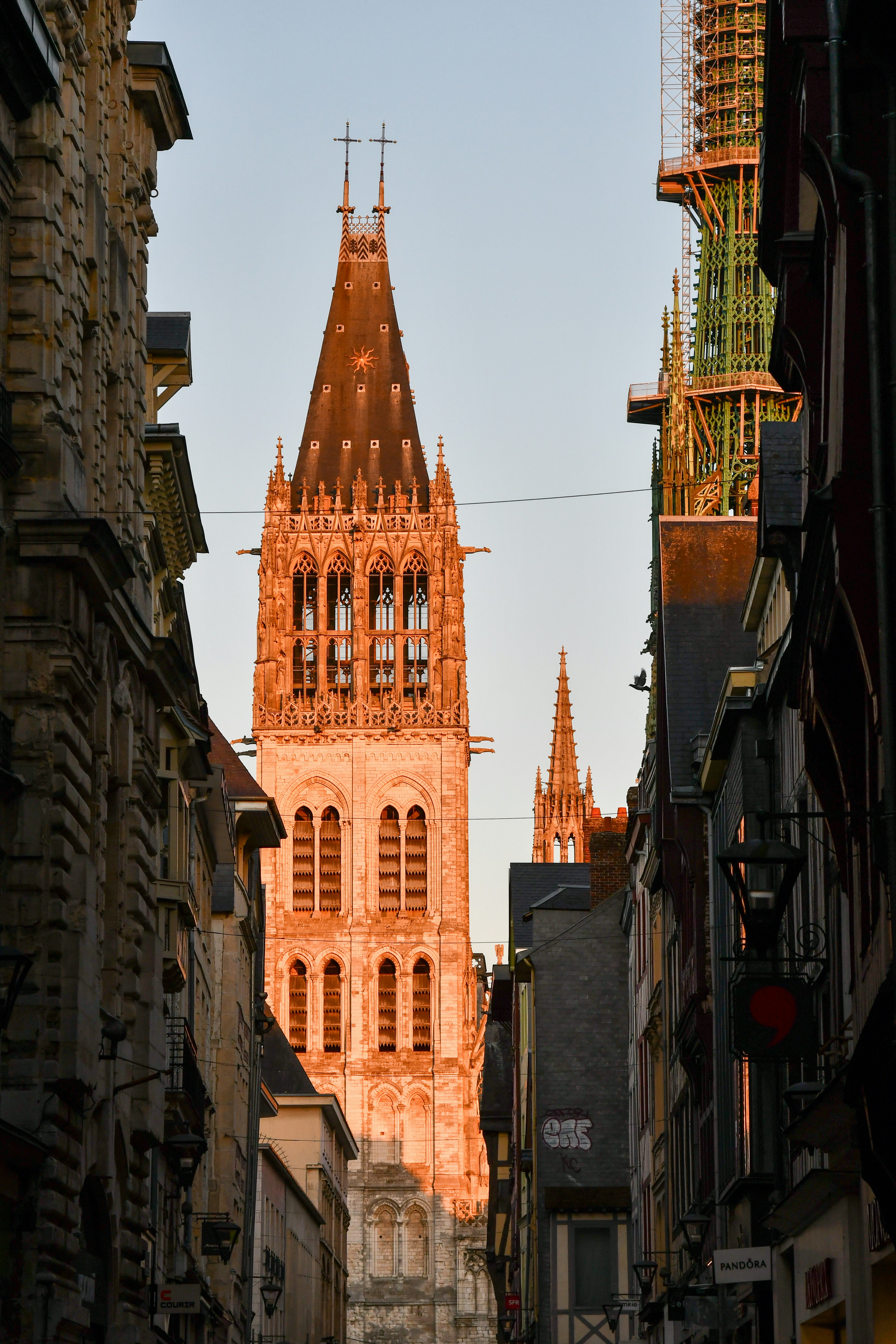 Ein hoher, gotischer Kirchturm, erleuchtet von warmem Licht am Ende einer Straße