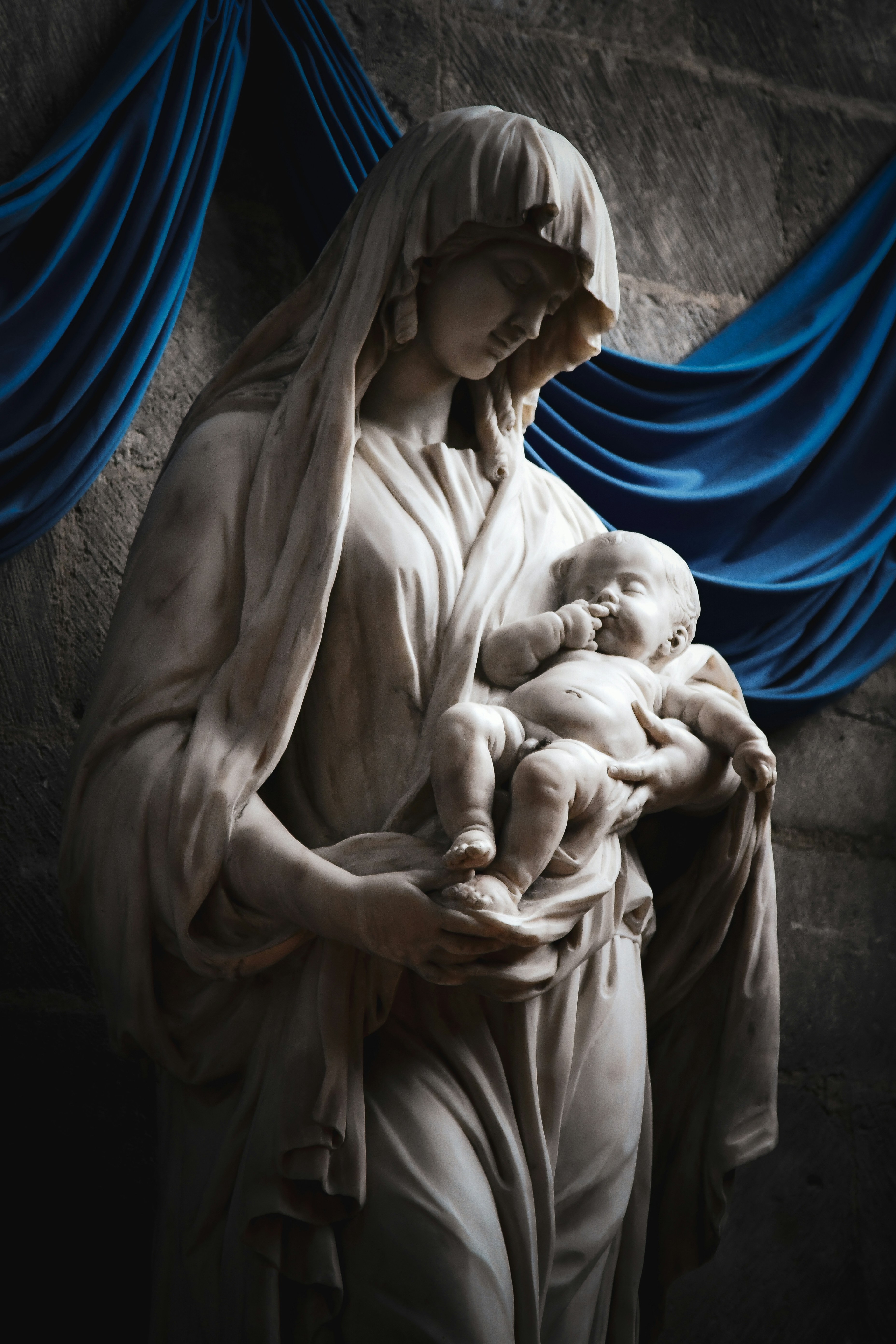 Eine Marmorstatue einer Frau, die ein Baby auf blau drapiertem Stoff hält