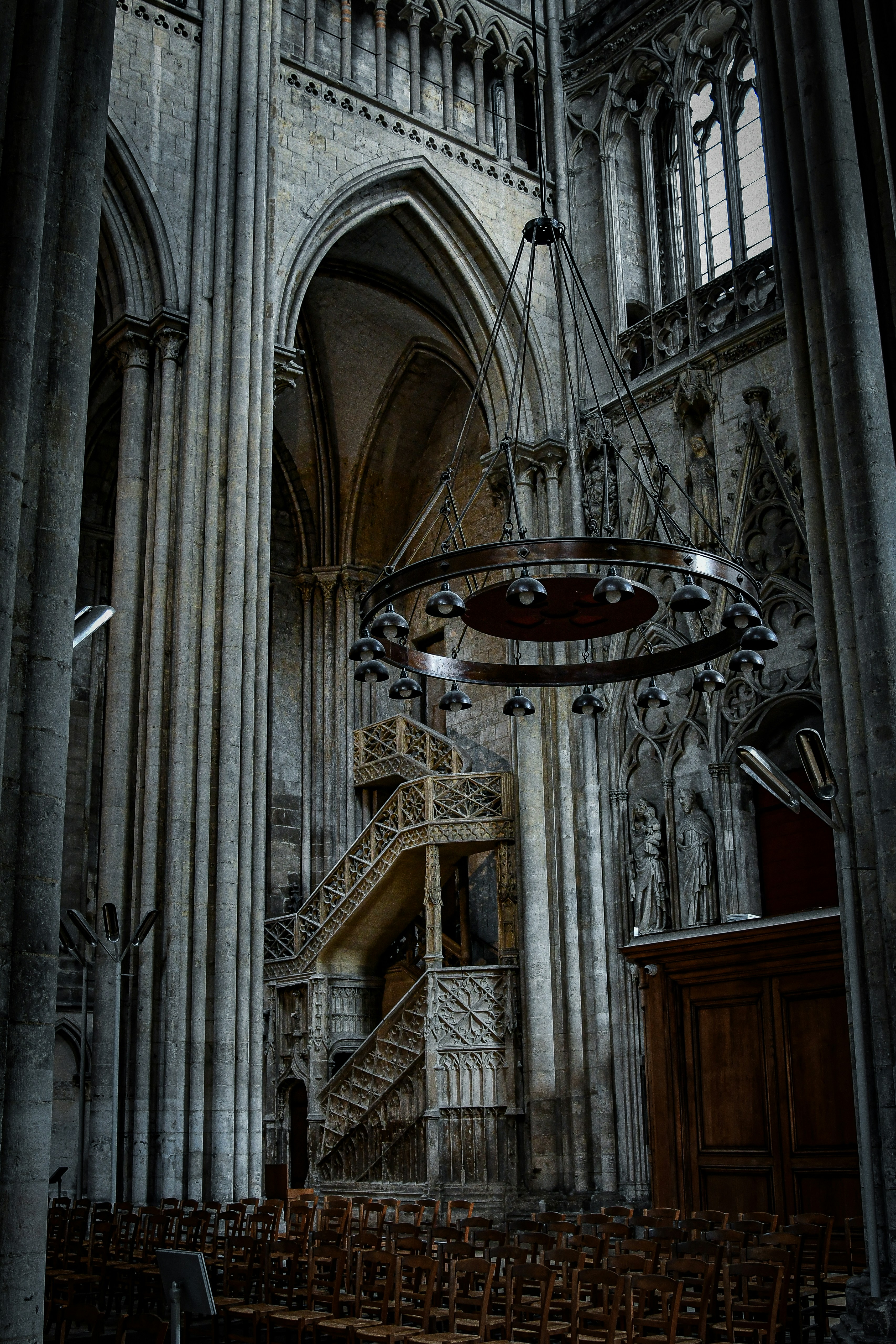 Ein großer, runder Kronleuchter hängt in einer gotischen Kathedrale mit Steinsäulen und Treppen