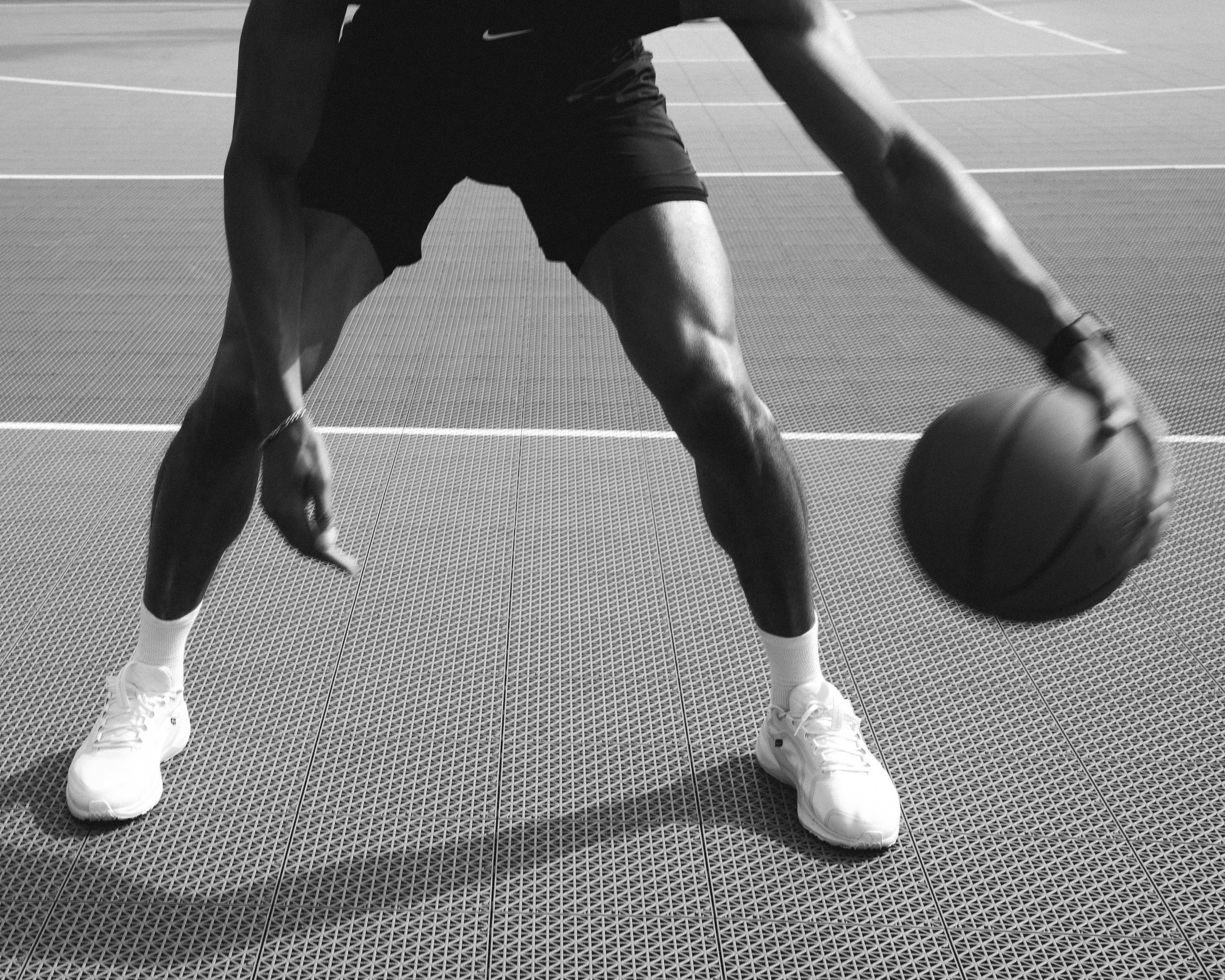 A person dribbling a basketball on an outdoor court in black and white
