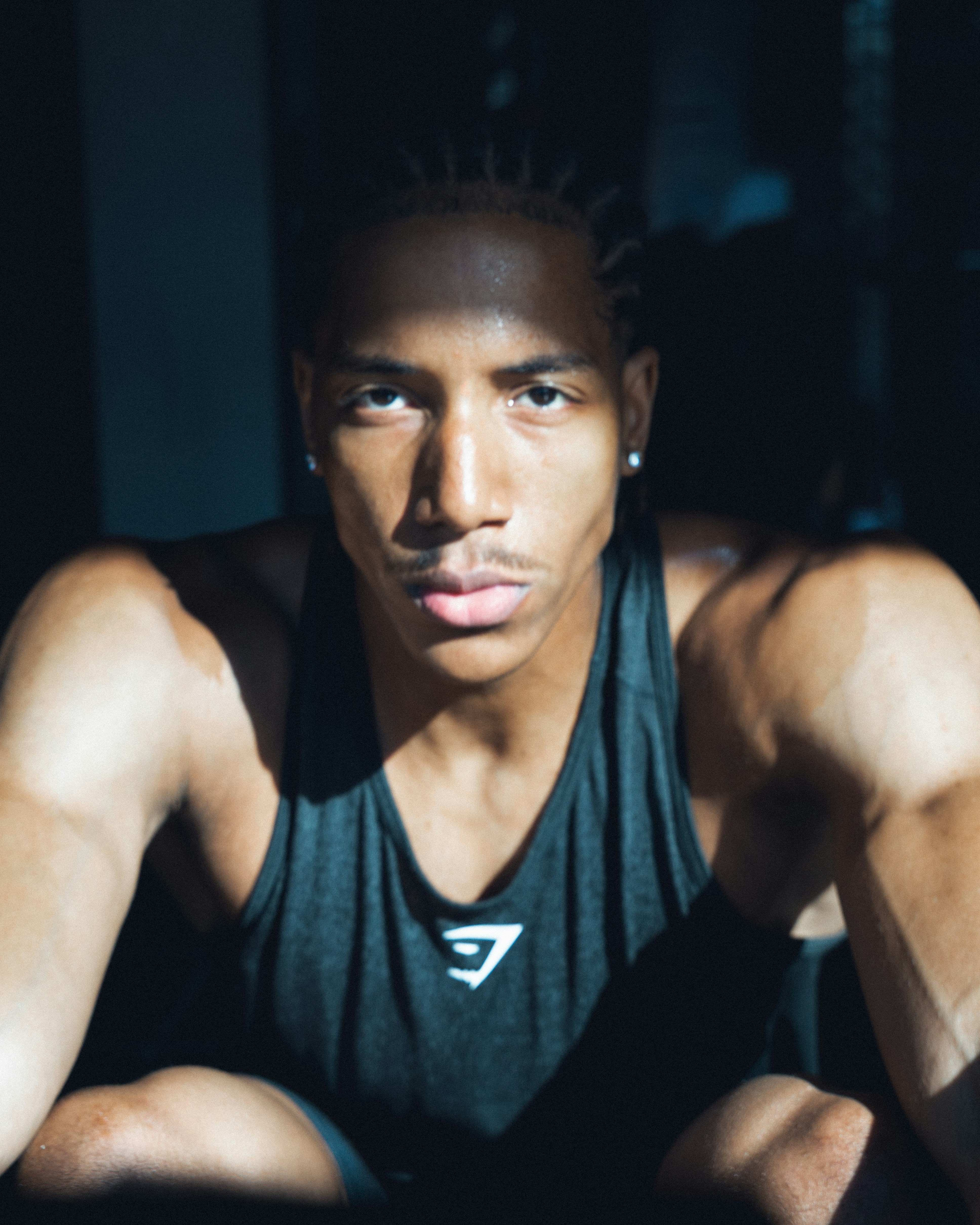 A man in a black tank top with braided hair in a gym