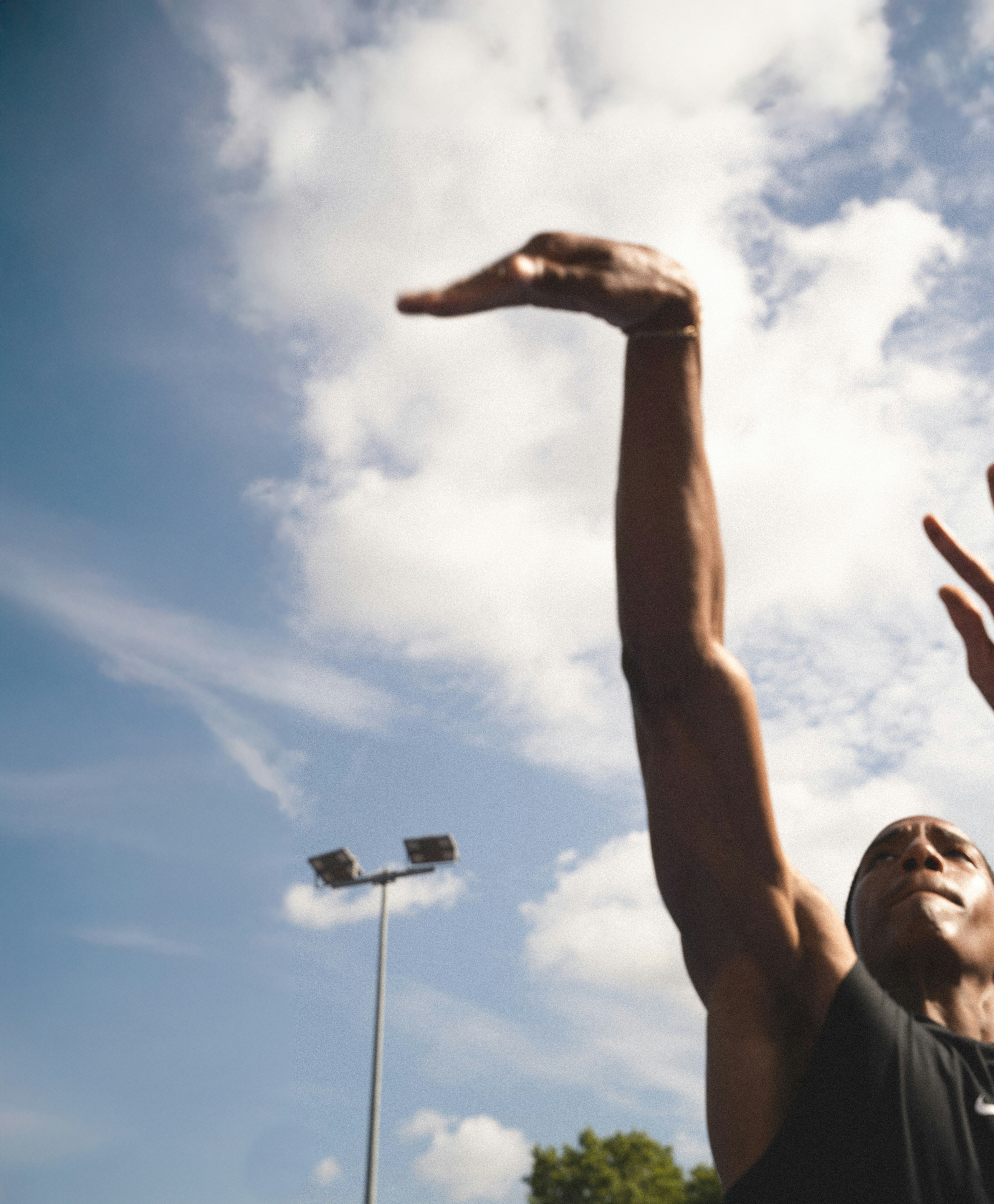 A person reaching an arm upward toward a blue sky with clouds