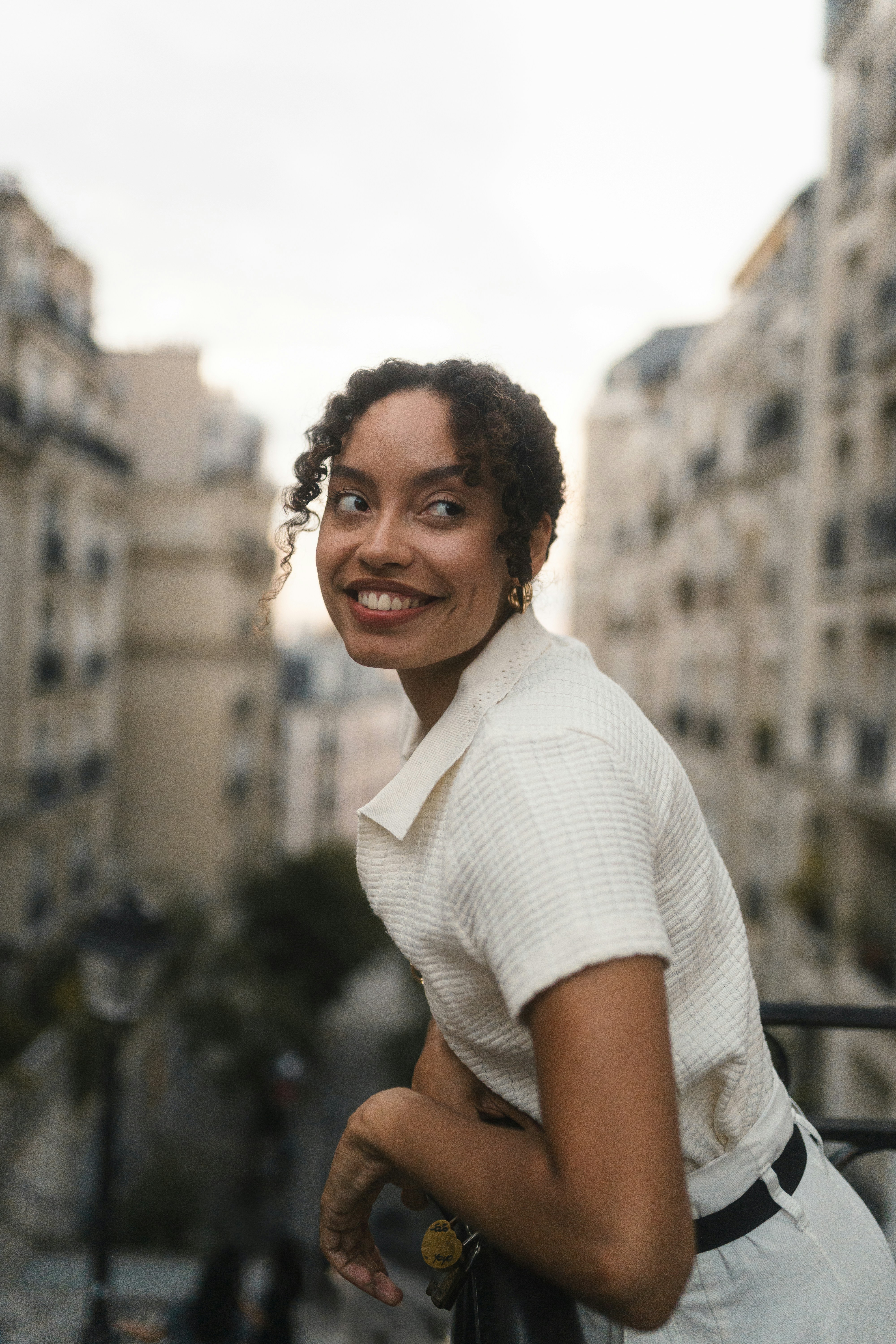 A woman in a white collared shirt leaning on a balcony in Paris
