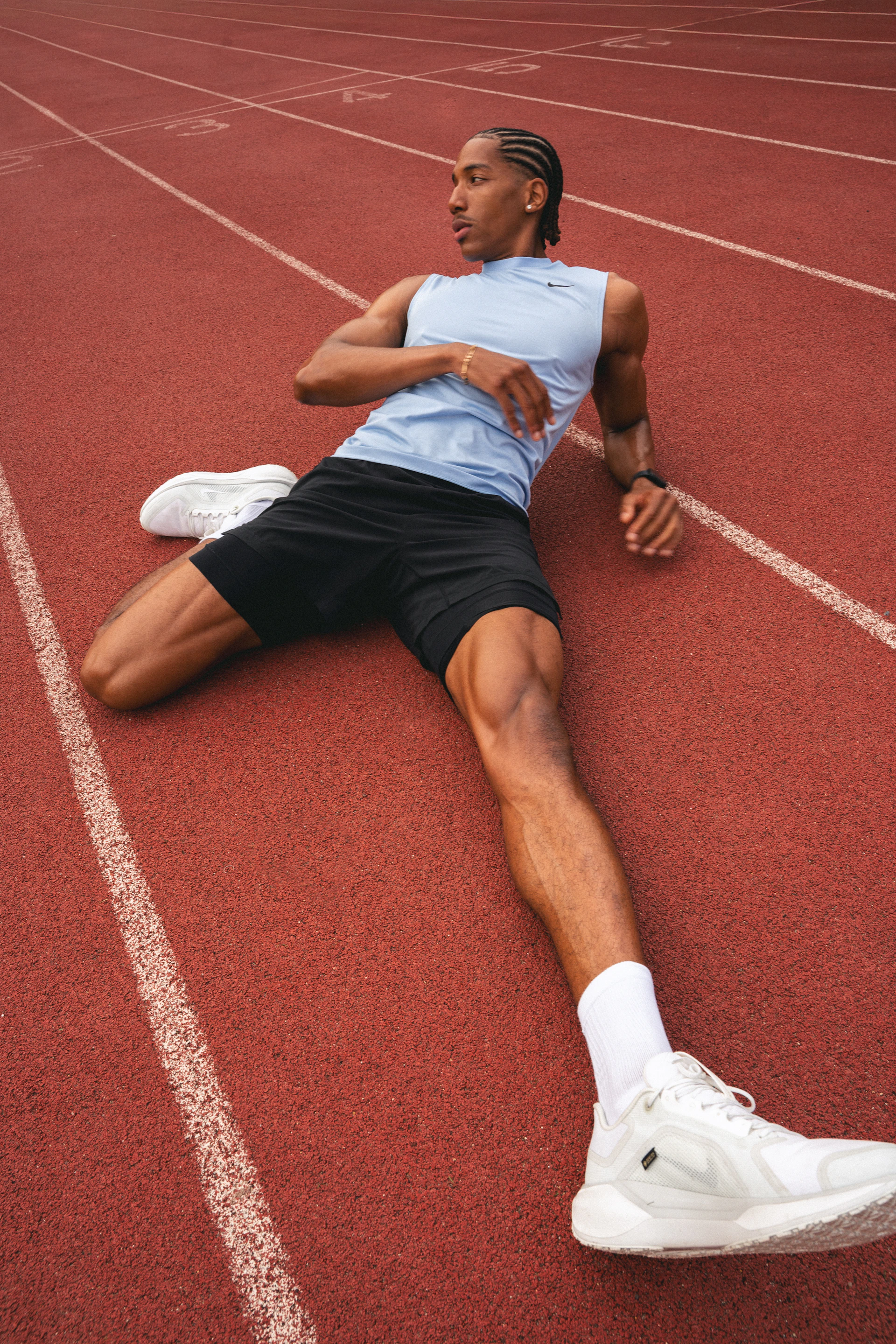 A man in a blue sleeveless top stretching on a red running track