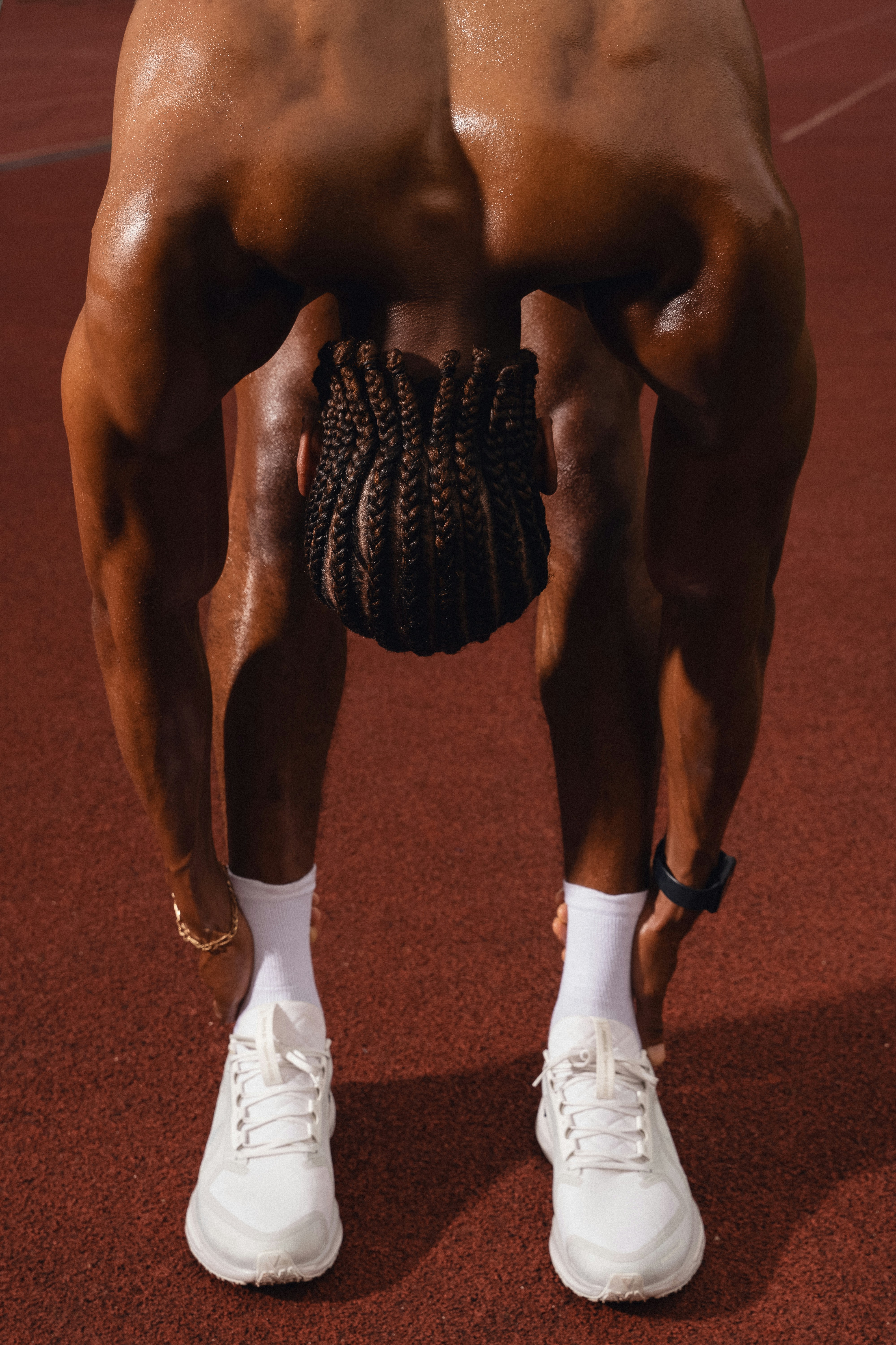 A person with braided hair stretching on a red running track