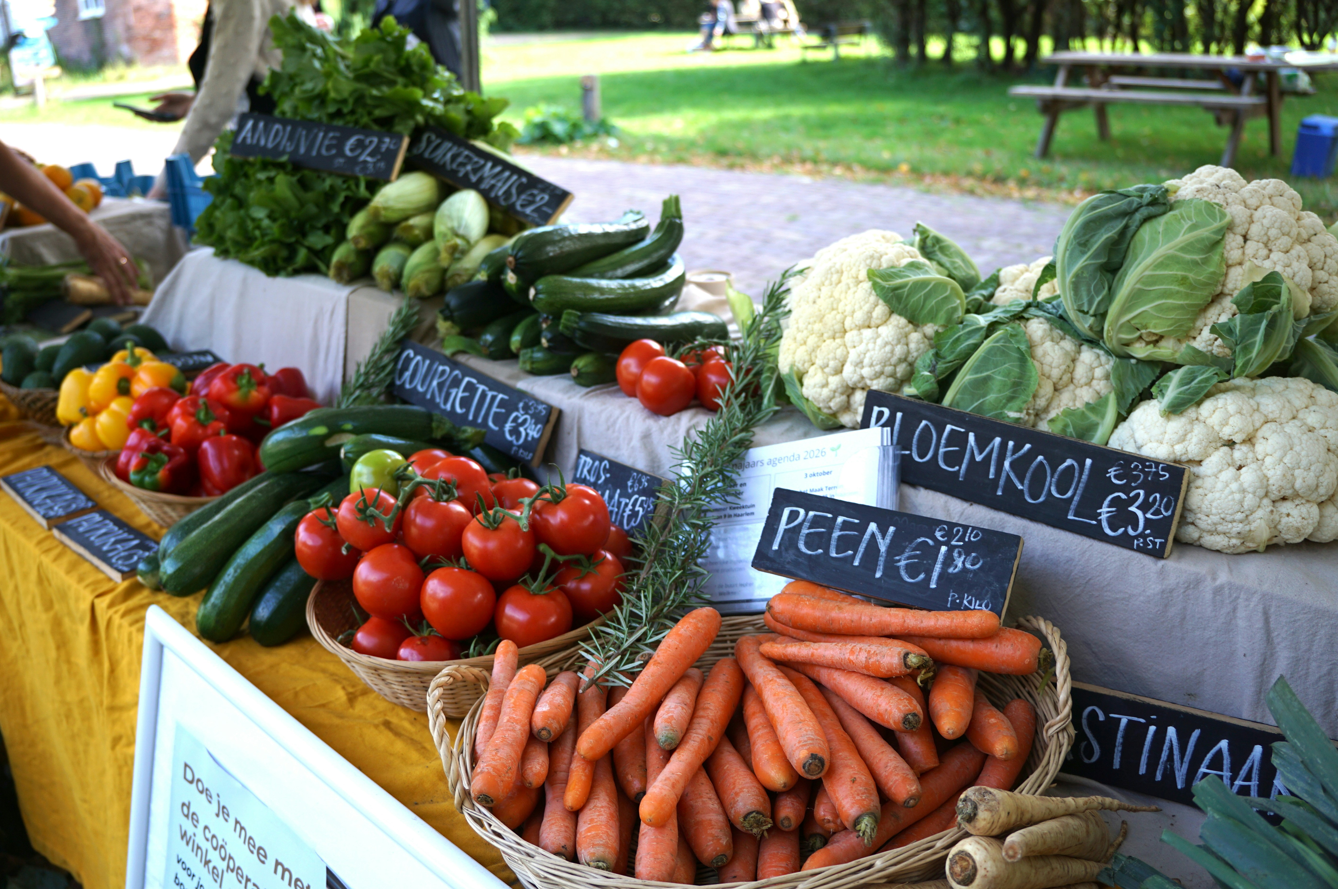 Fresh vegetables including carrots, tomatoes, cauliflower, and zucchini at an outdoor market stall