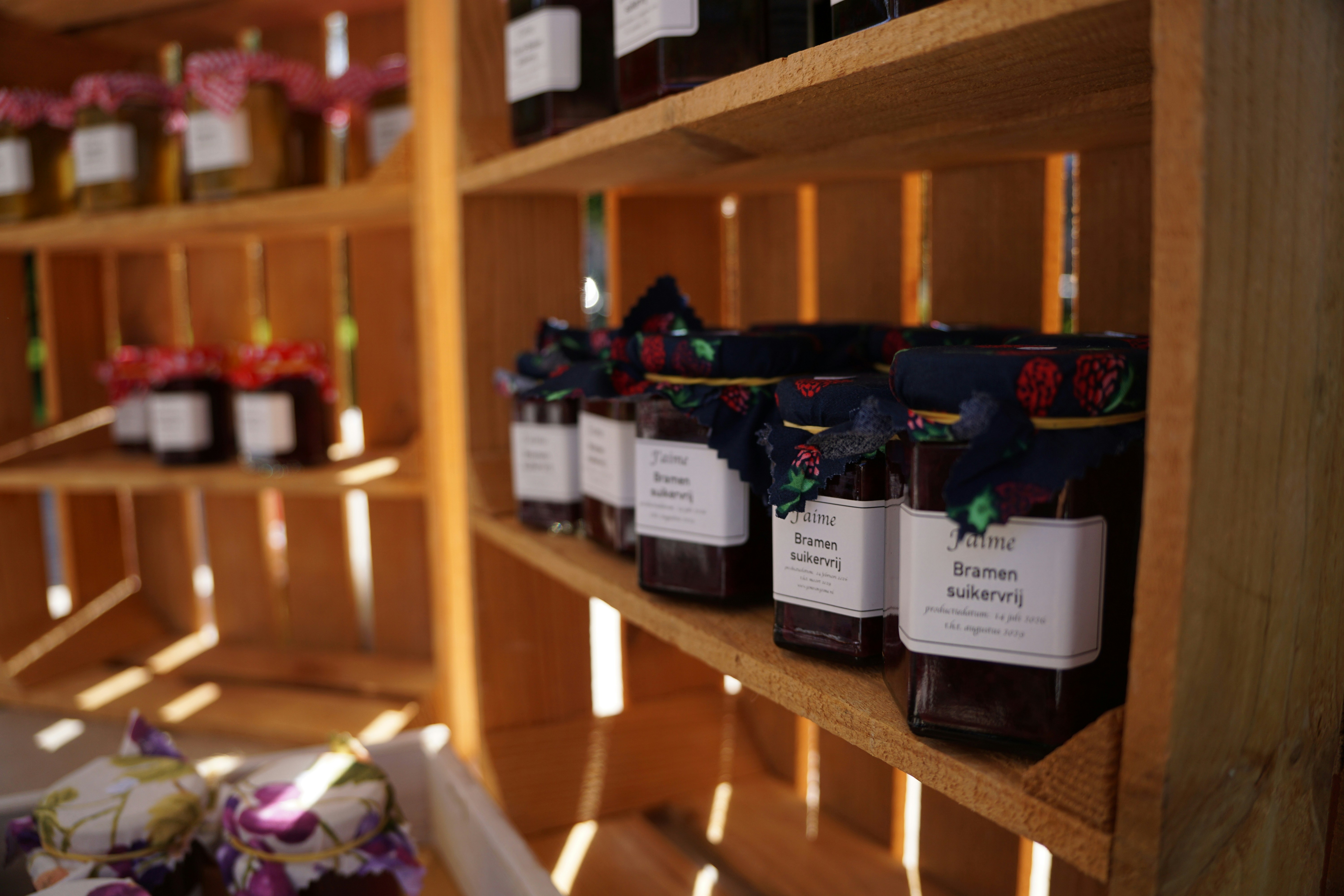 Glass jars of jam with fabric lids on wooden shelves in a market