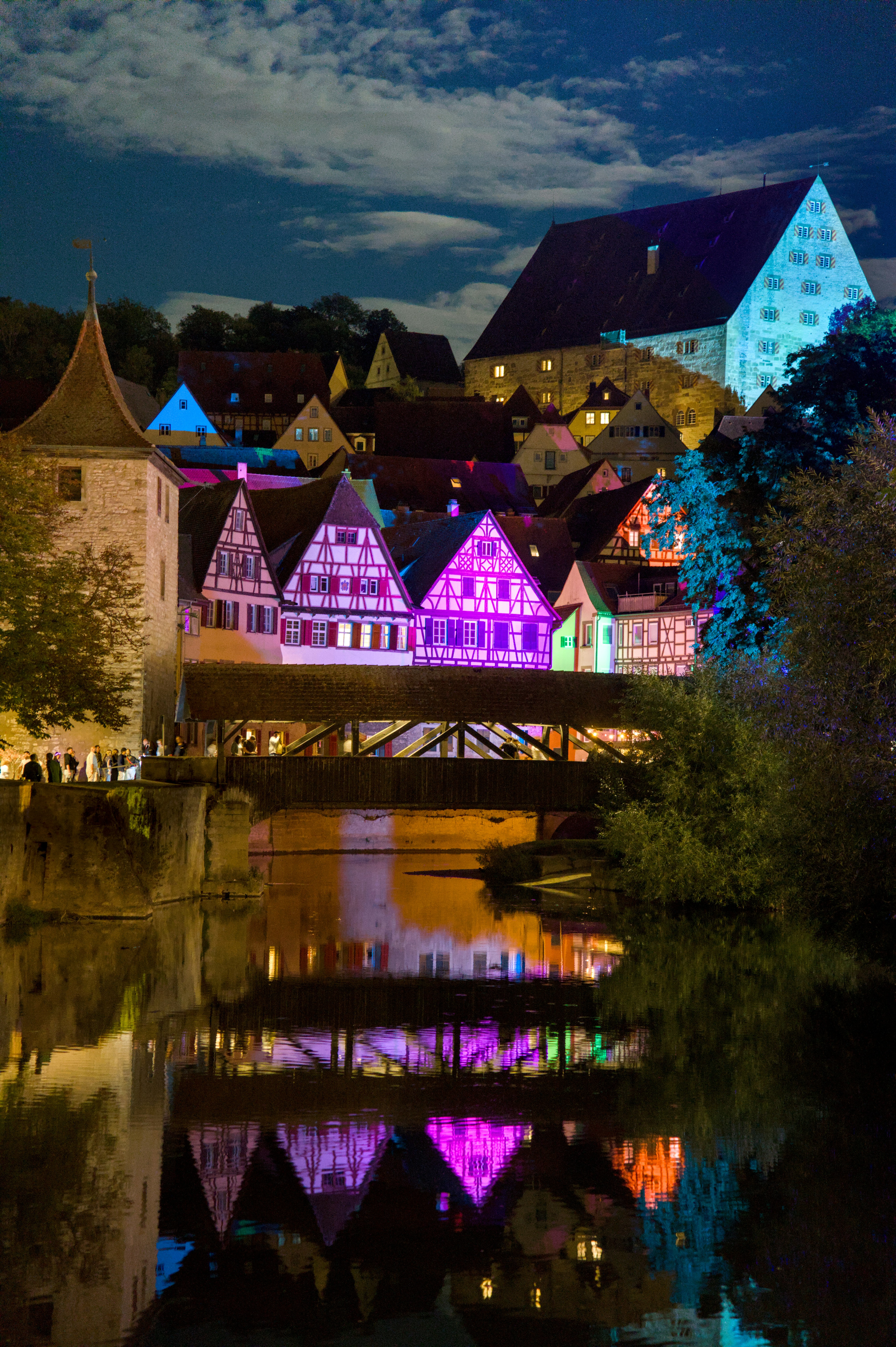 Half-timbered houses illuminated in vibrant colors reflecting in a river at night