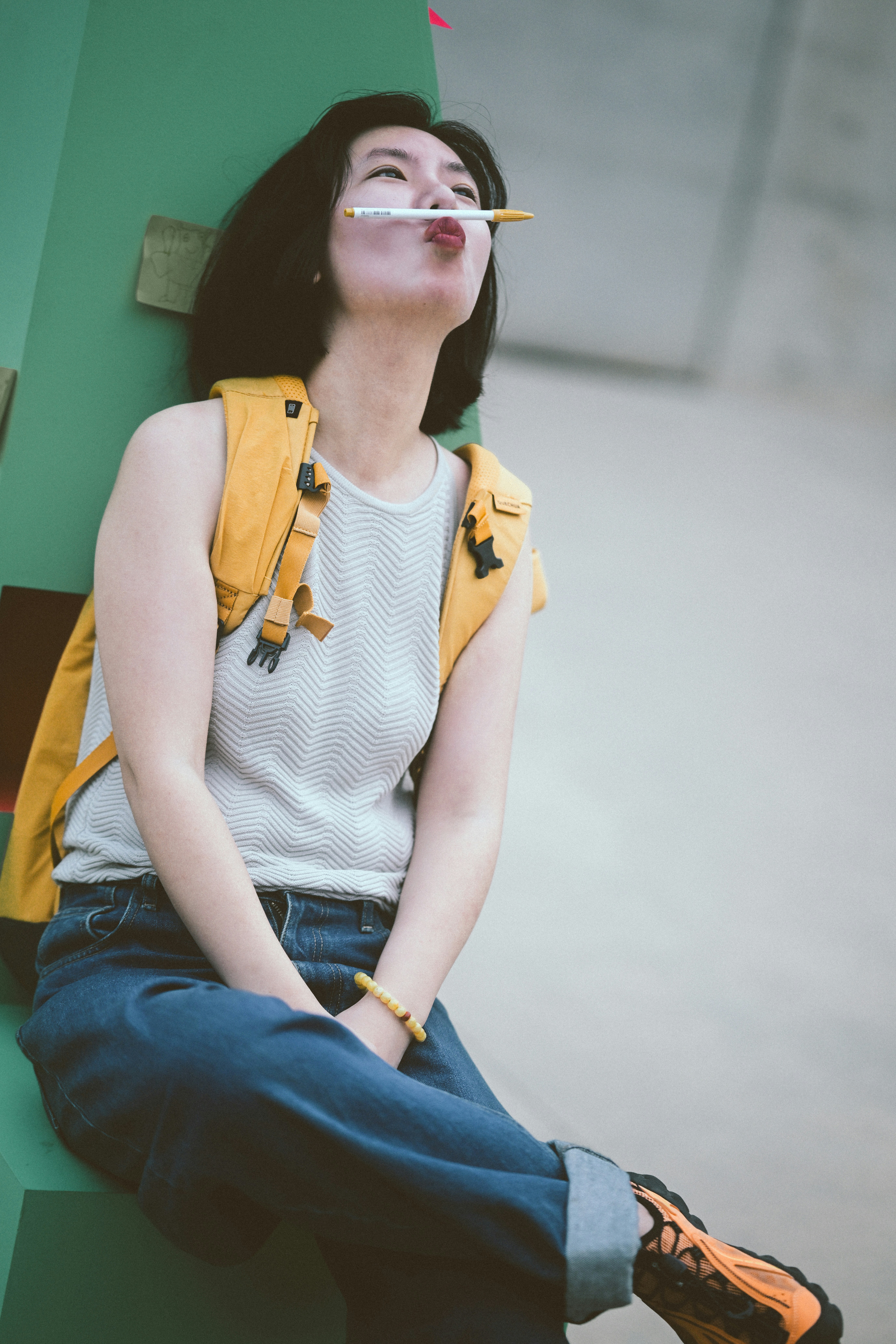 A woman with a pen between her nose and lips wearing a yellow backpack
