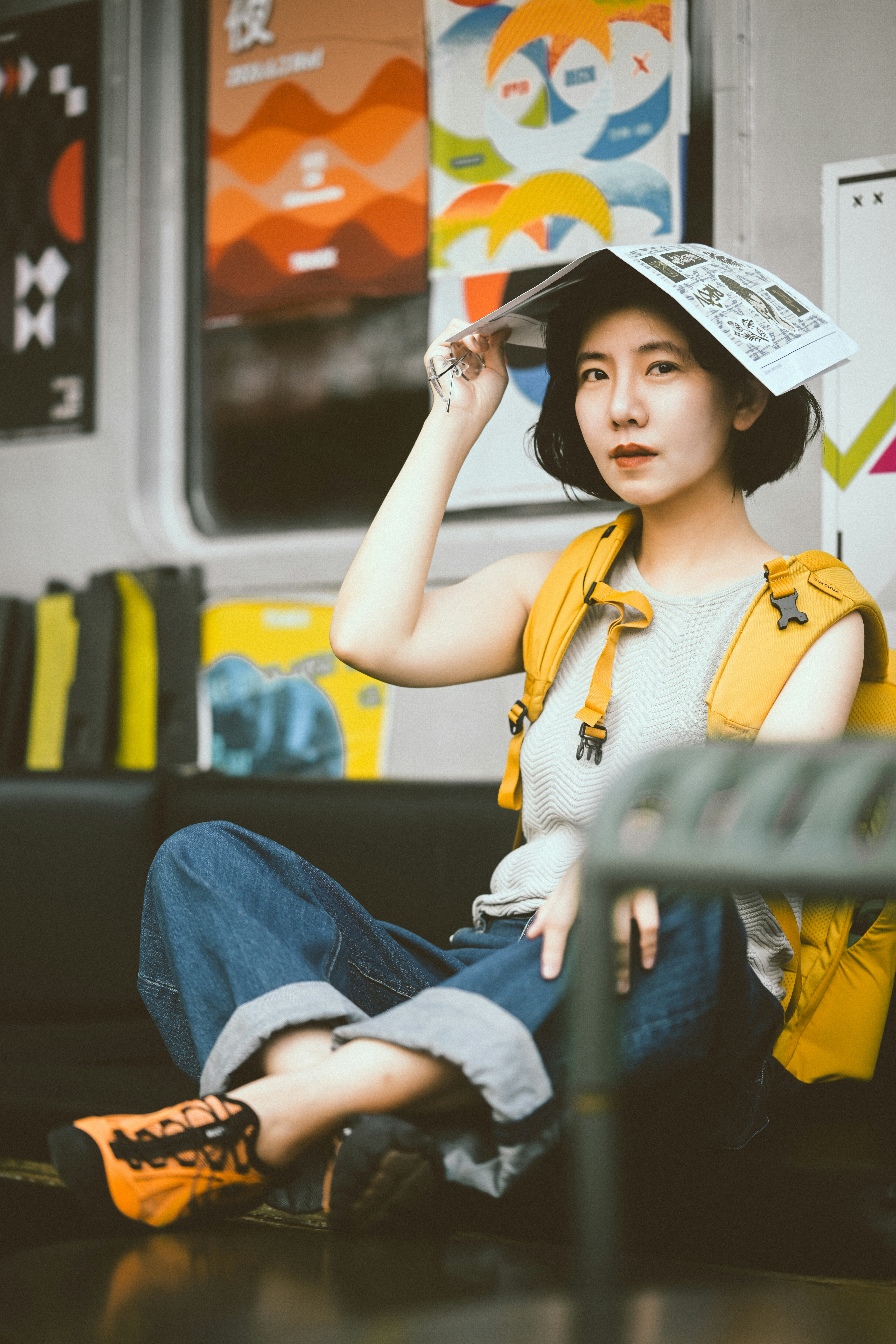 A woman with a yellow backpack holding a newspaper over her head on a train