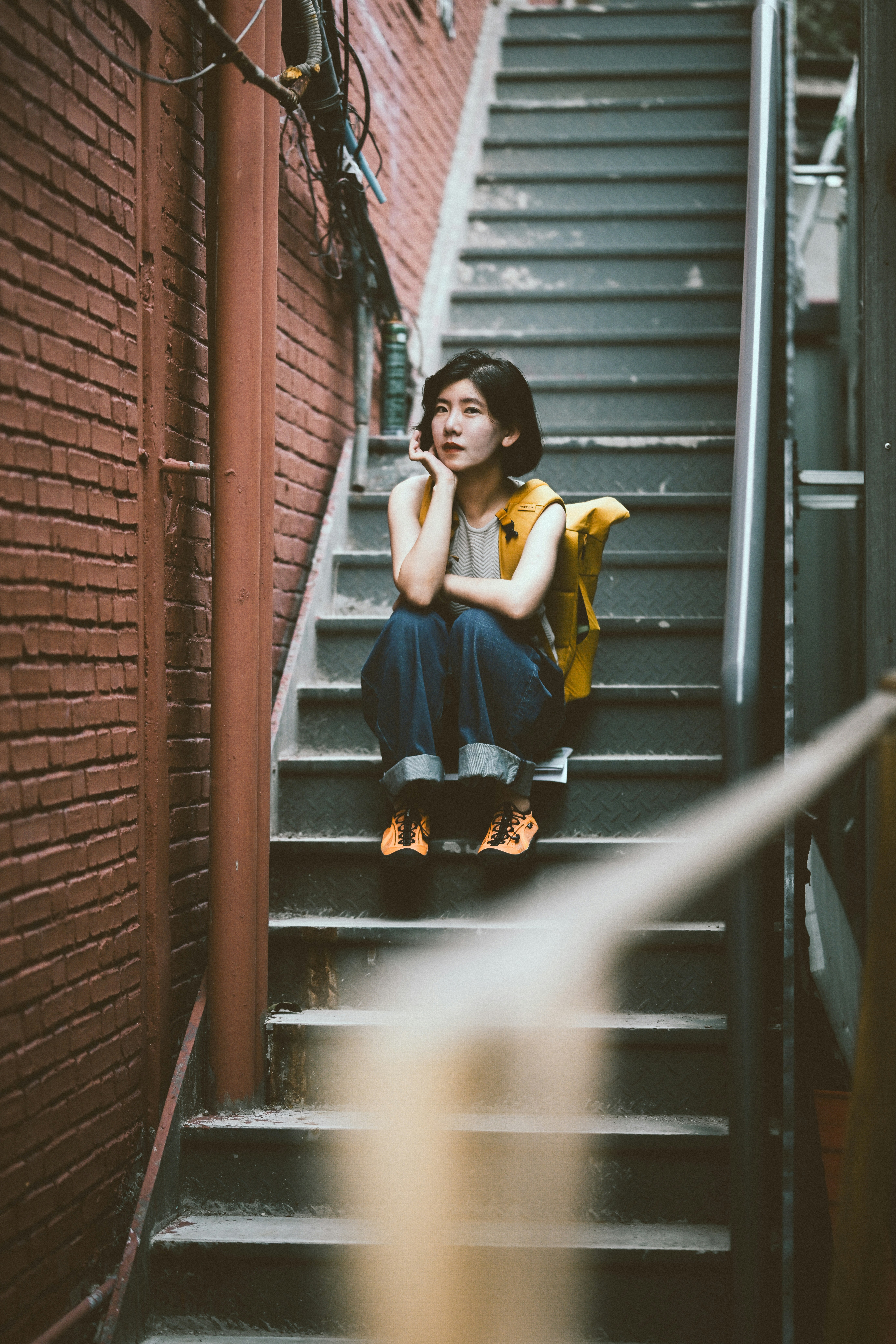 A woman with a yellow backpack sitting on metal stairs between brick walls
