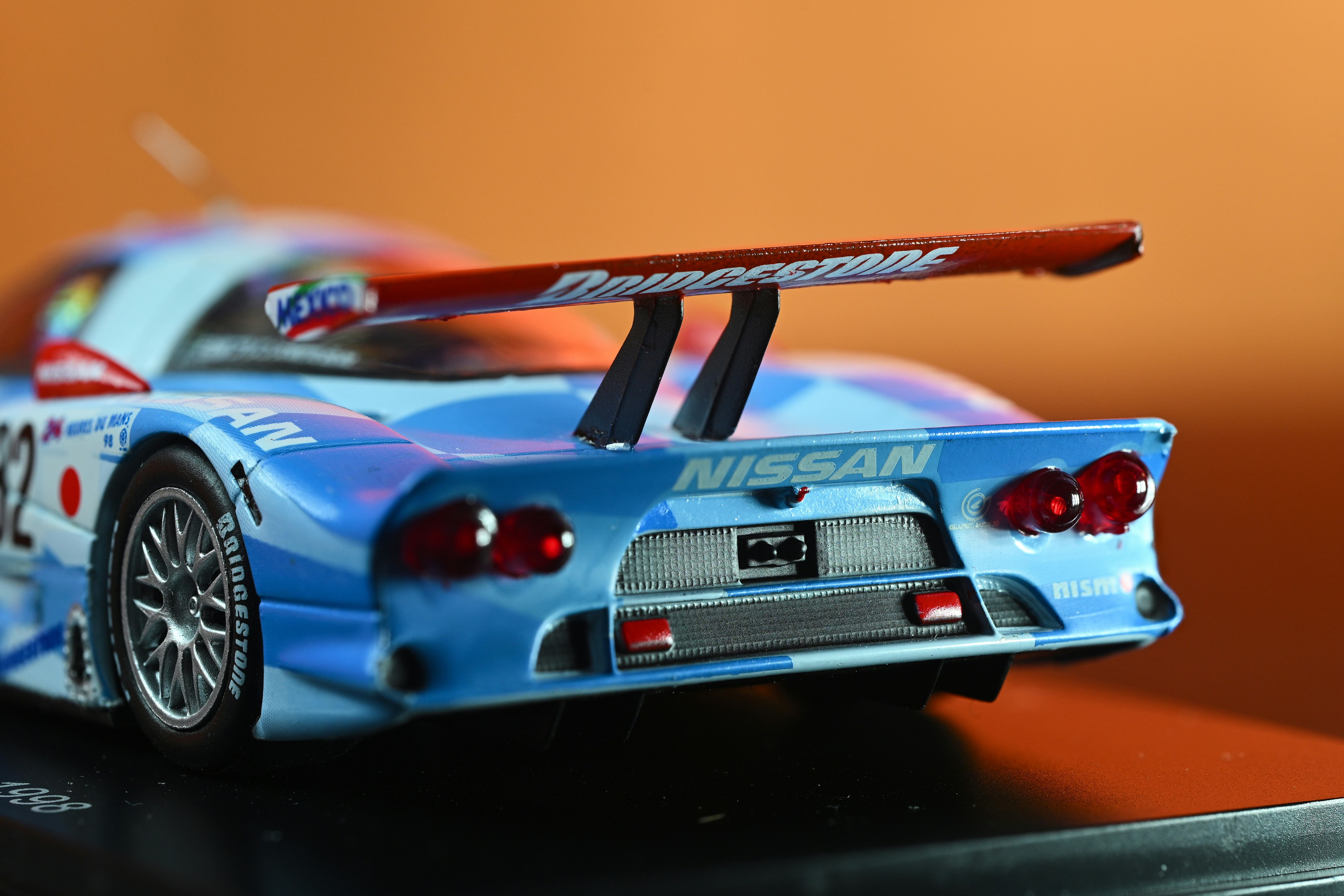 A blue Nissan race car model with a large rear spoiler on a stand