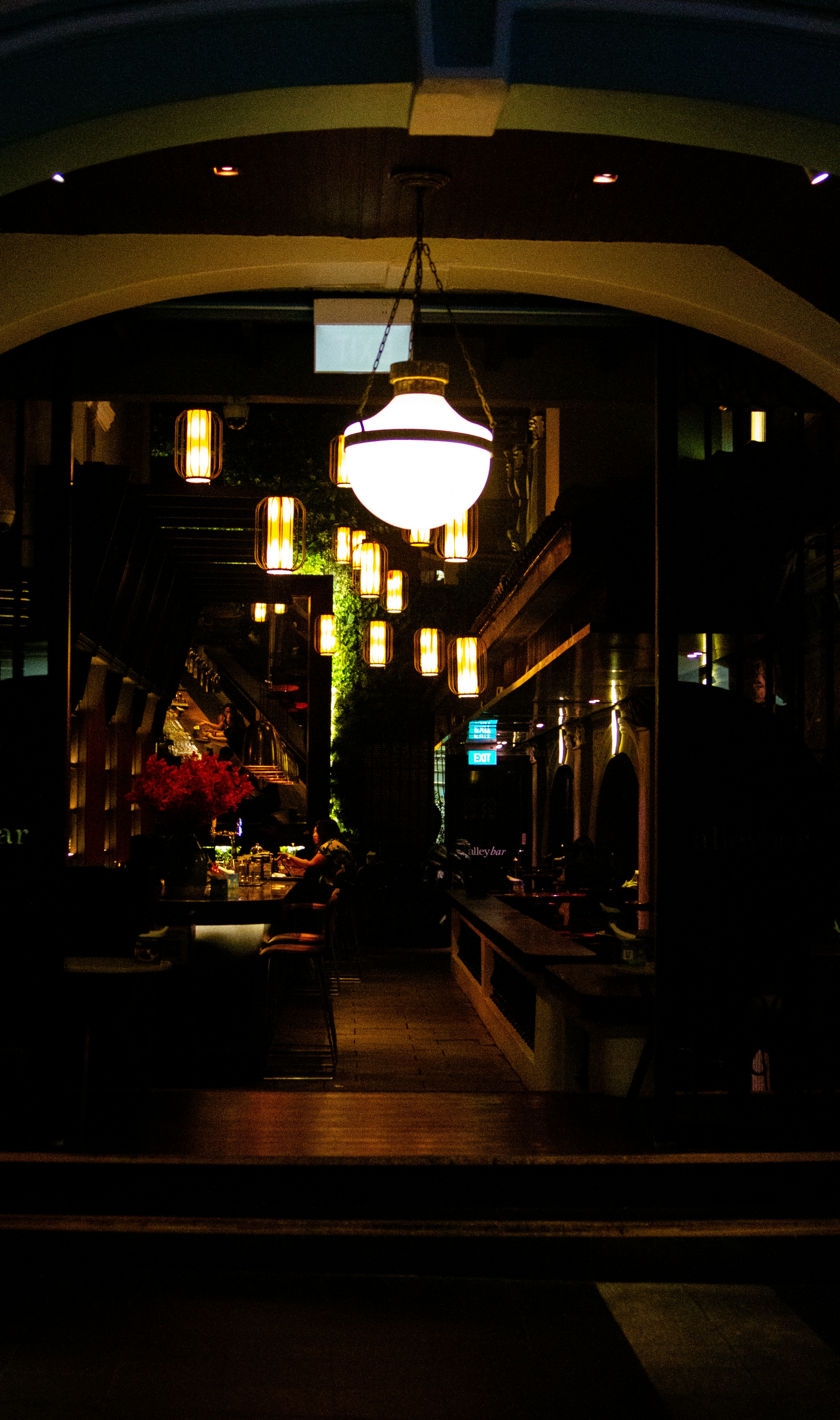 A dimly lit bar interior with hanging lanterns and a person at the counter
