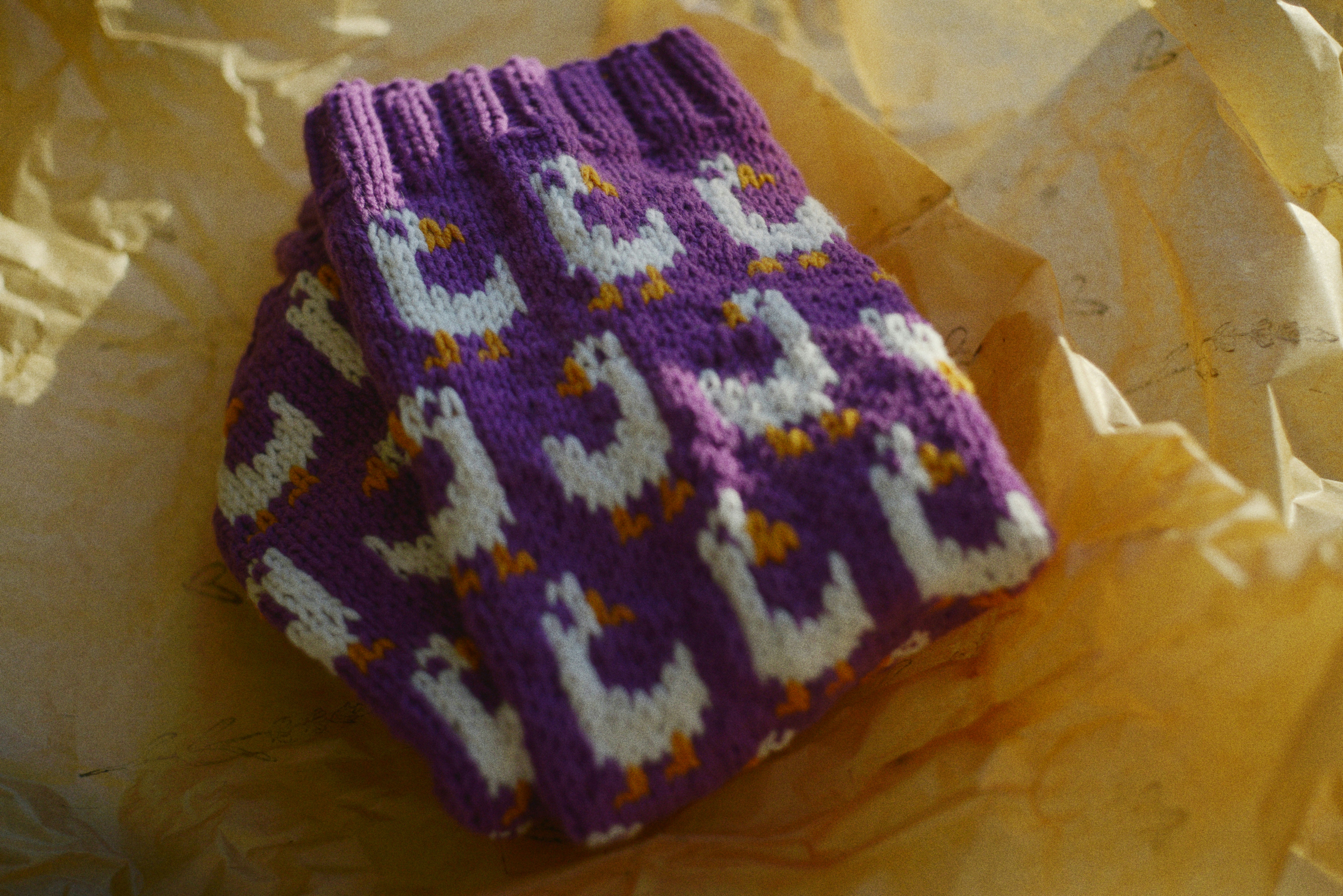 A pair of purple knitted socks with a white goose pattern on crumpled paper