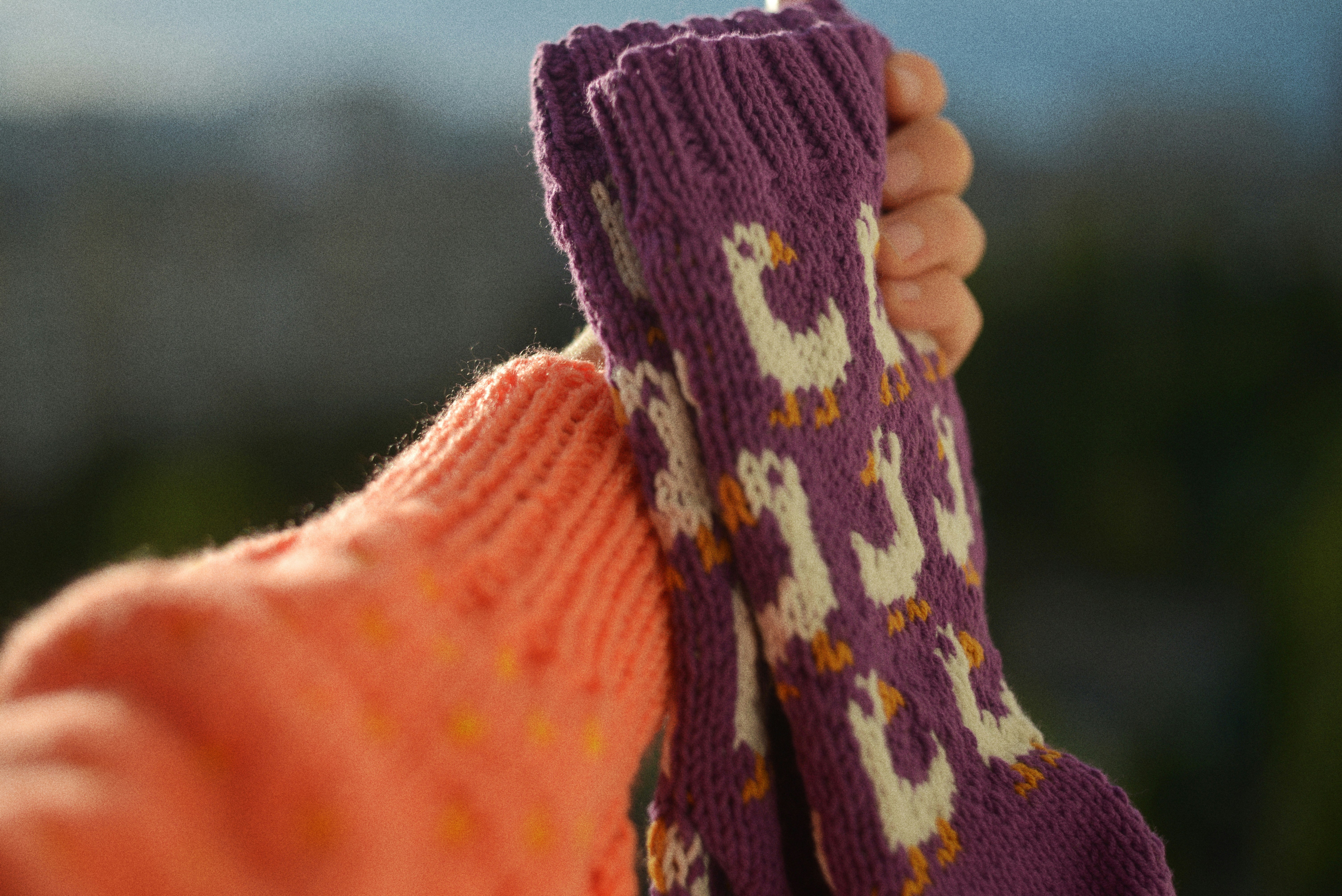 A person wearing a peach sweater holding up a purple sock with goose patterns