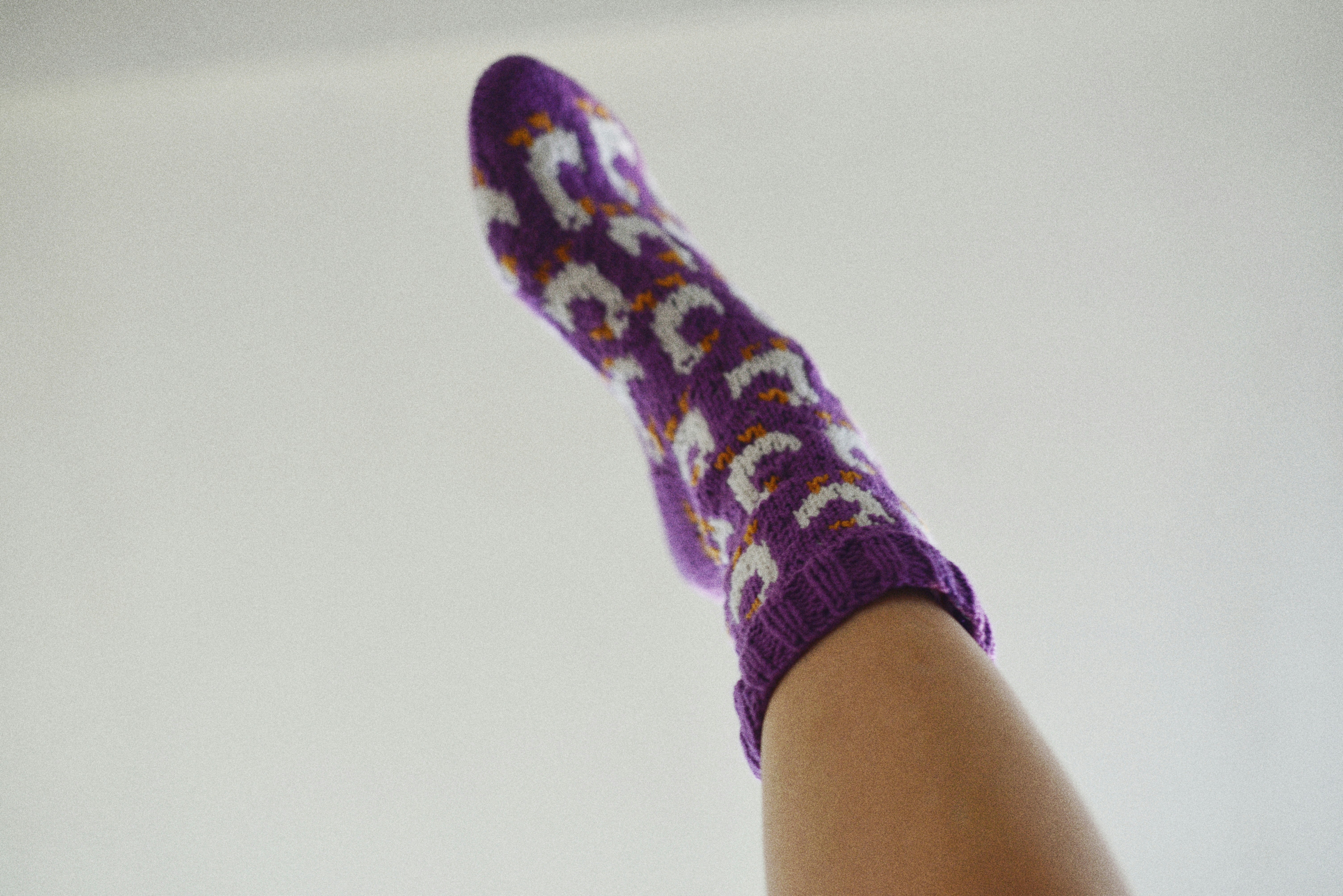A person wearing a purple knitted sock with a white and orange pattern