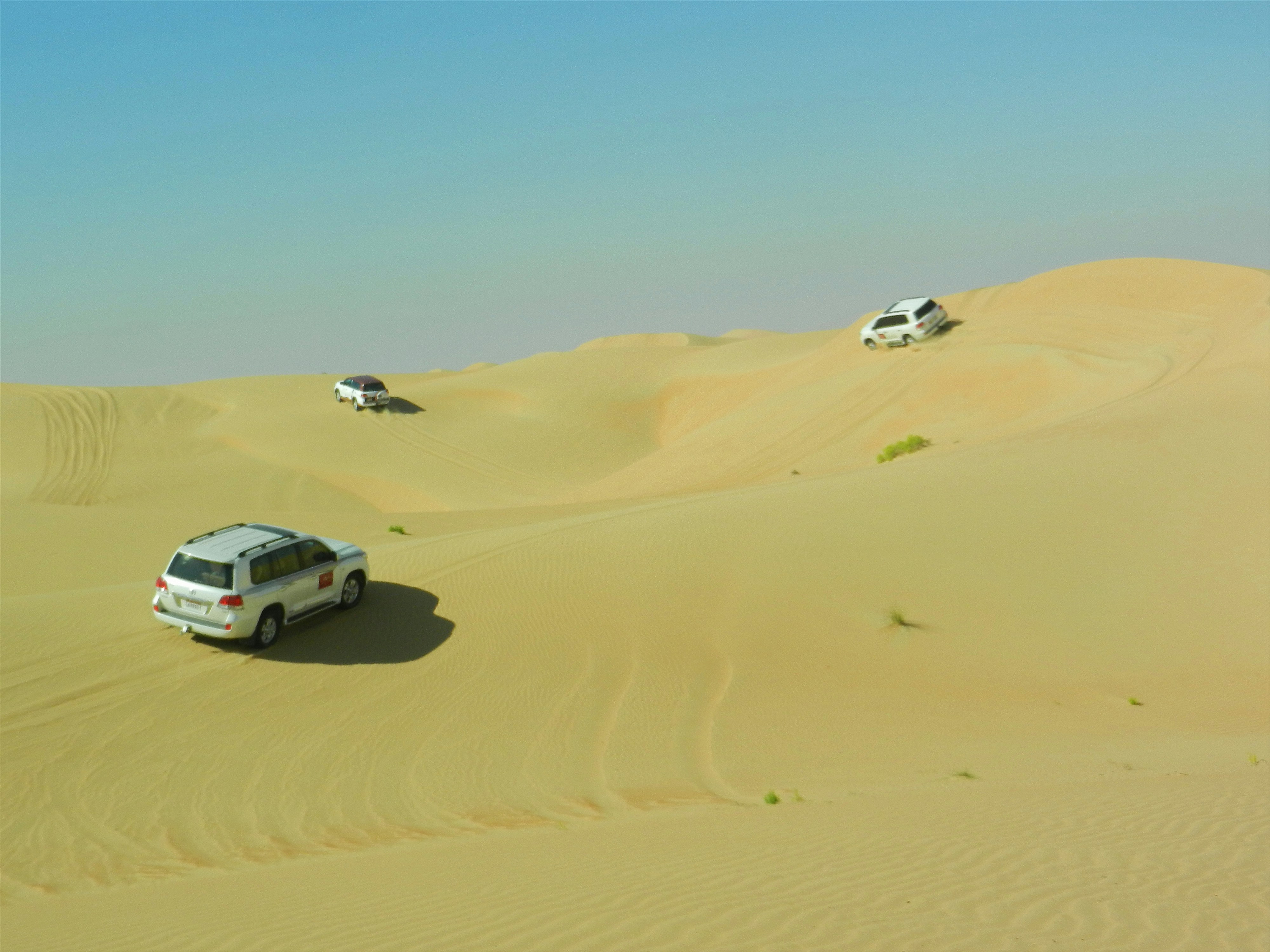Three white off-road vehicles driving across rolling sand dunes in a desert
