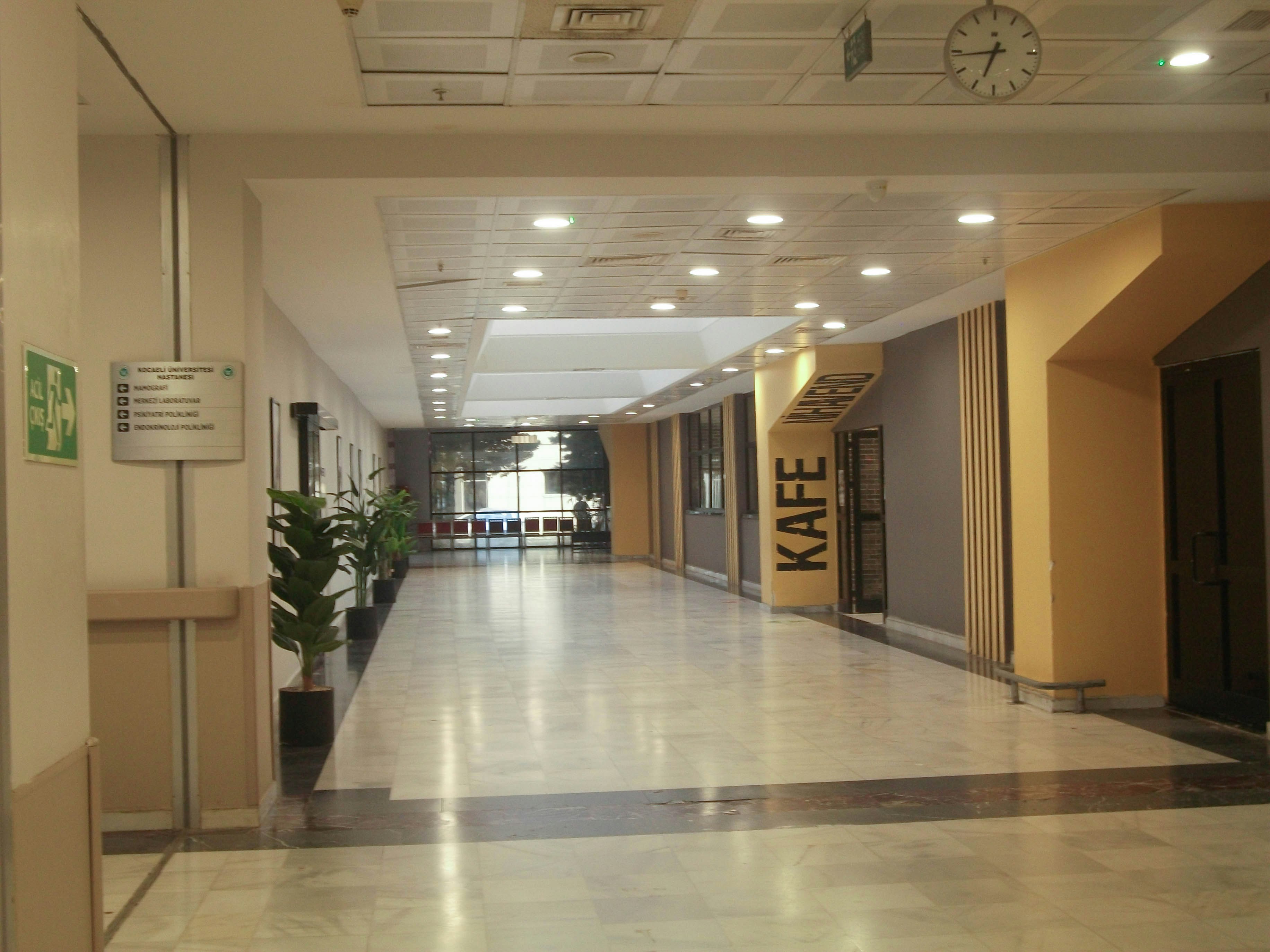 A wide hospital corridor with marble floors, potted plants, and a cafe sign