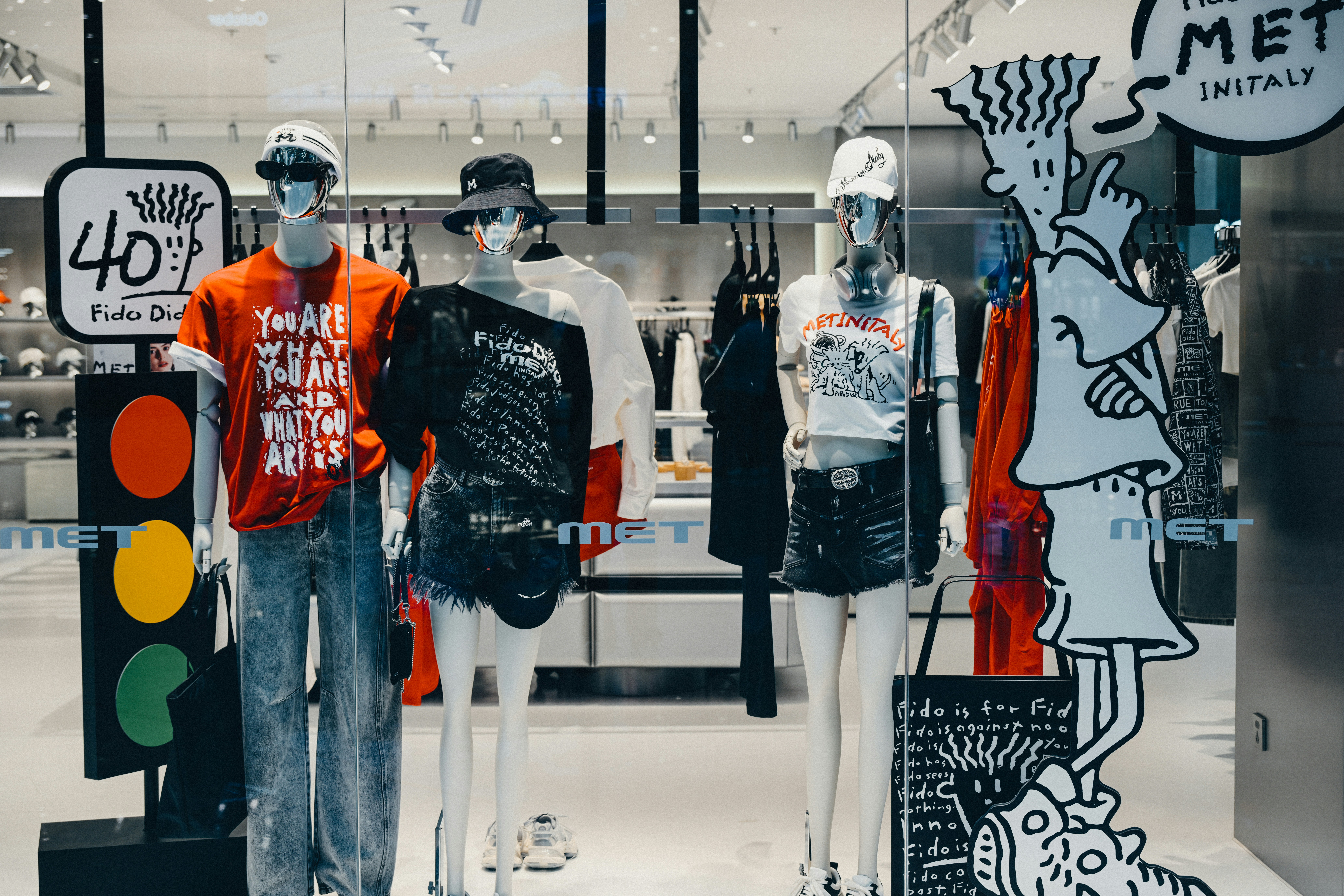 Three mannequins wearing casual clothing in a brightly lit clothing store window display