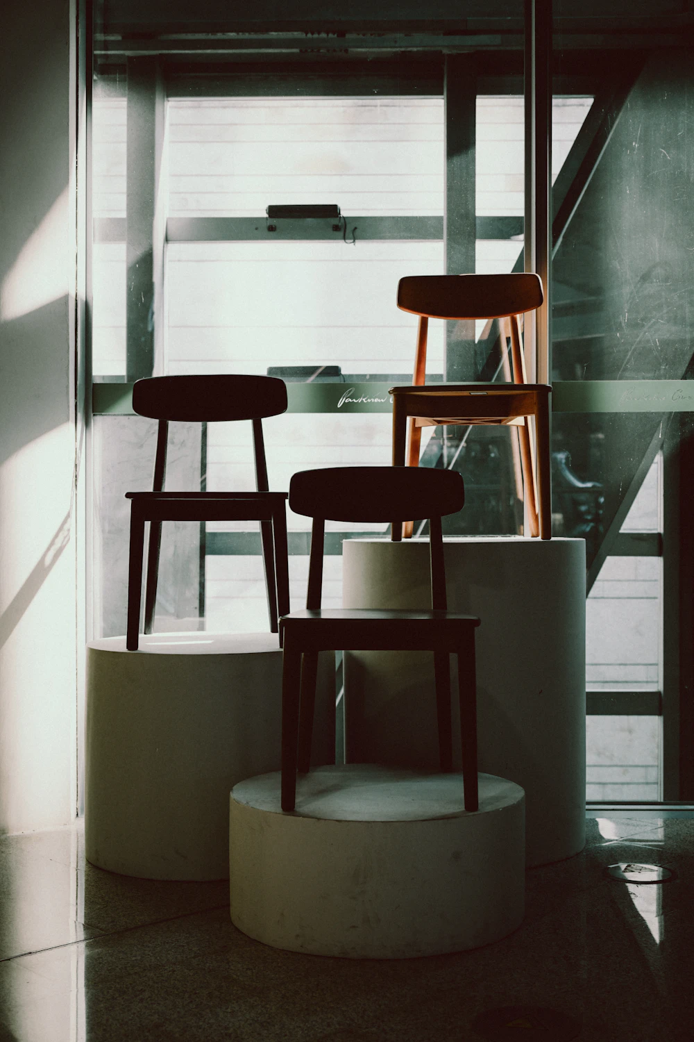 Three designer chairs displayed on cylindrical pedestals beside a window