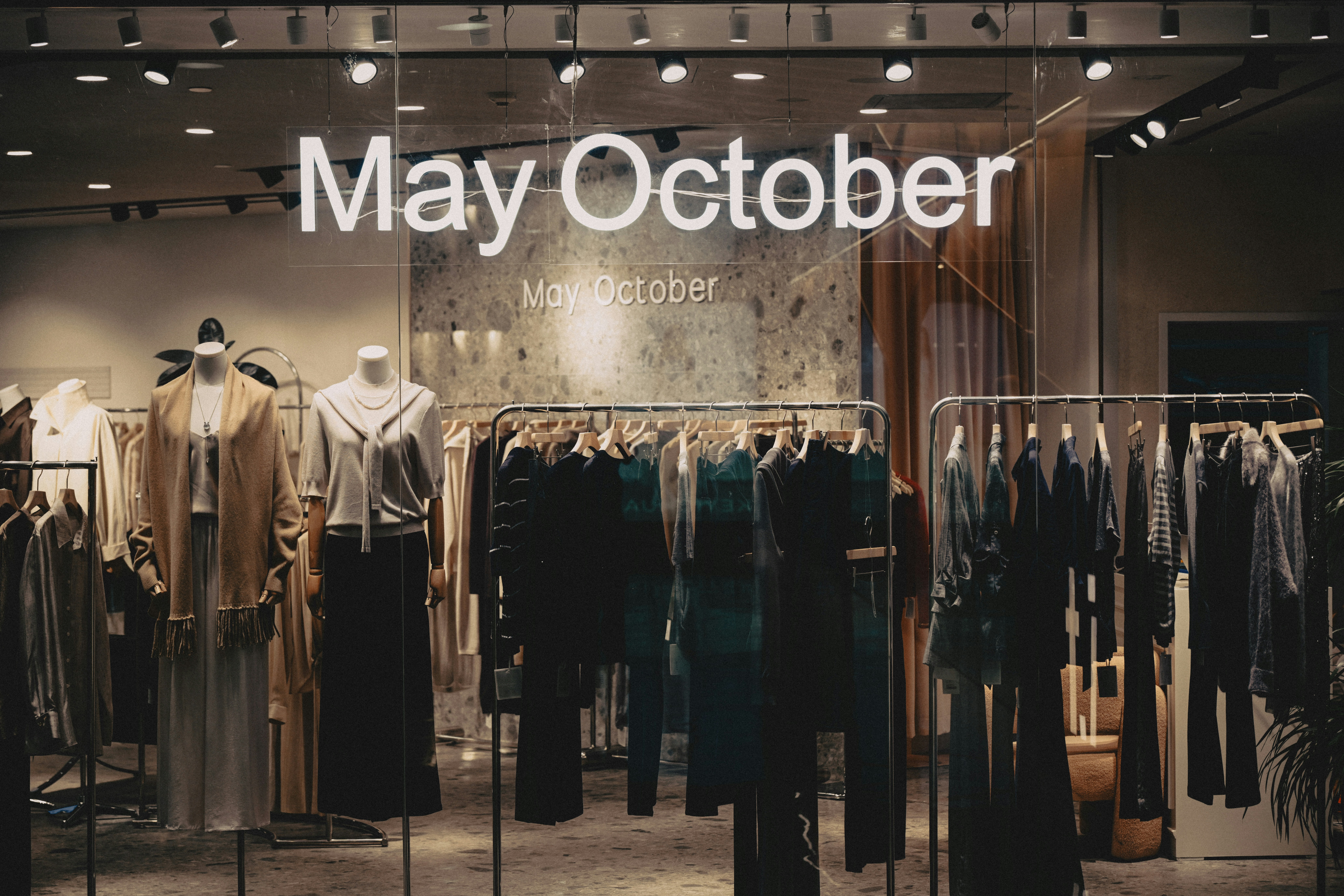 Clothing store window display with mannequins and racks of garments under warm lighting