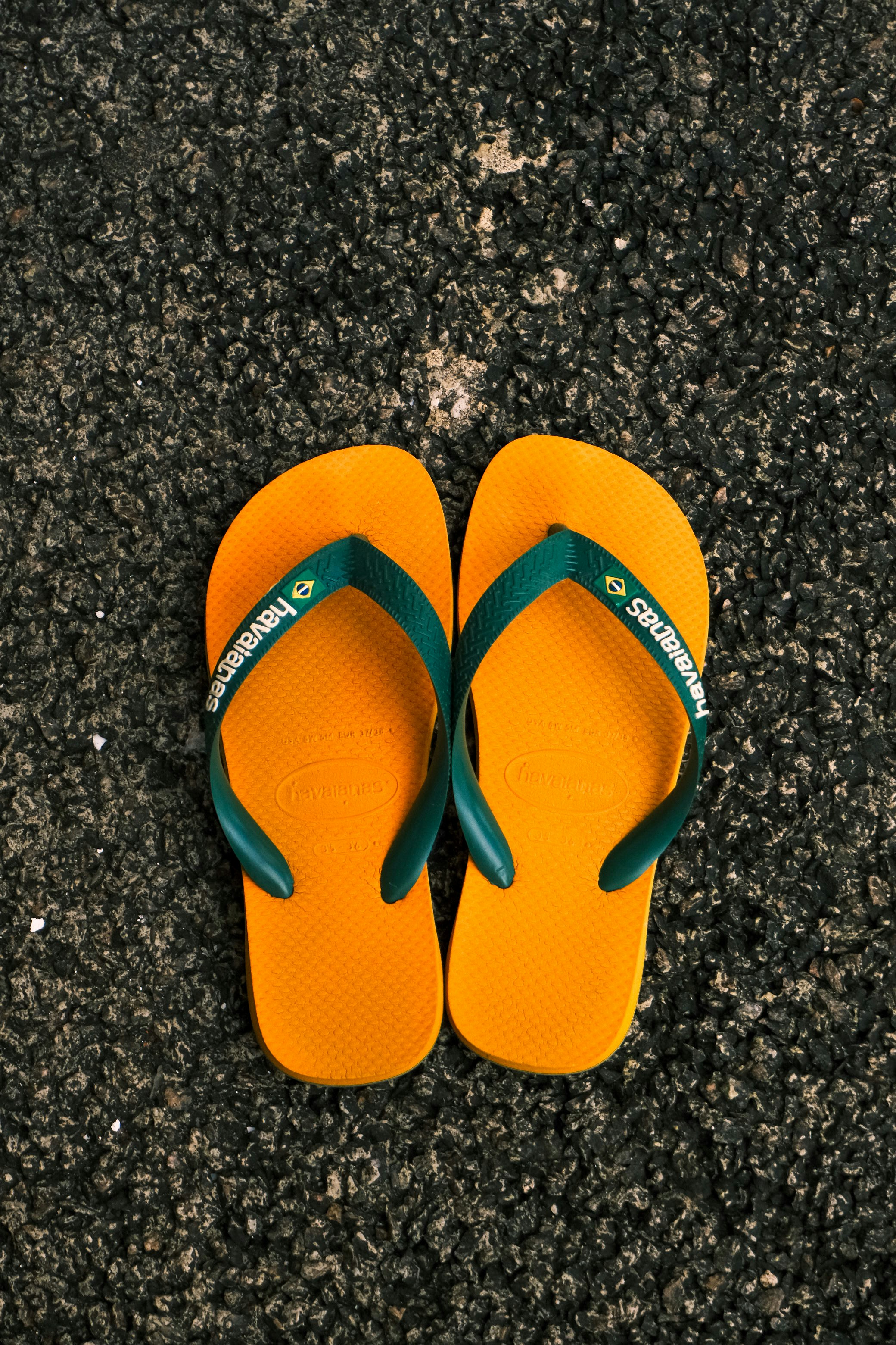 A pair of yellow flip-flops with green straps on dark asphalt