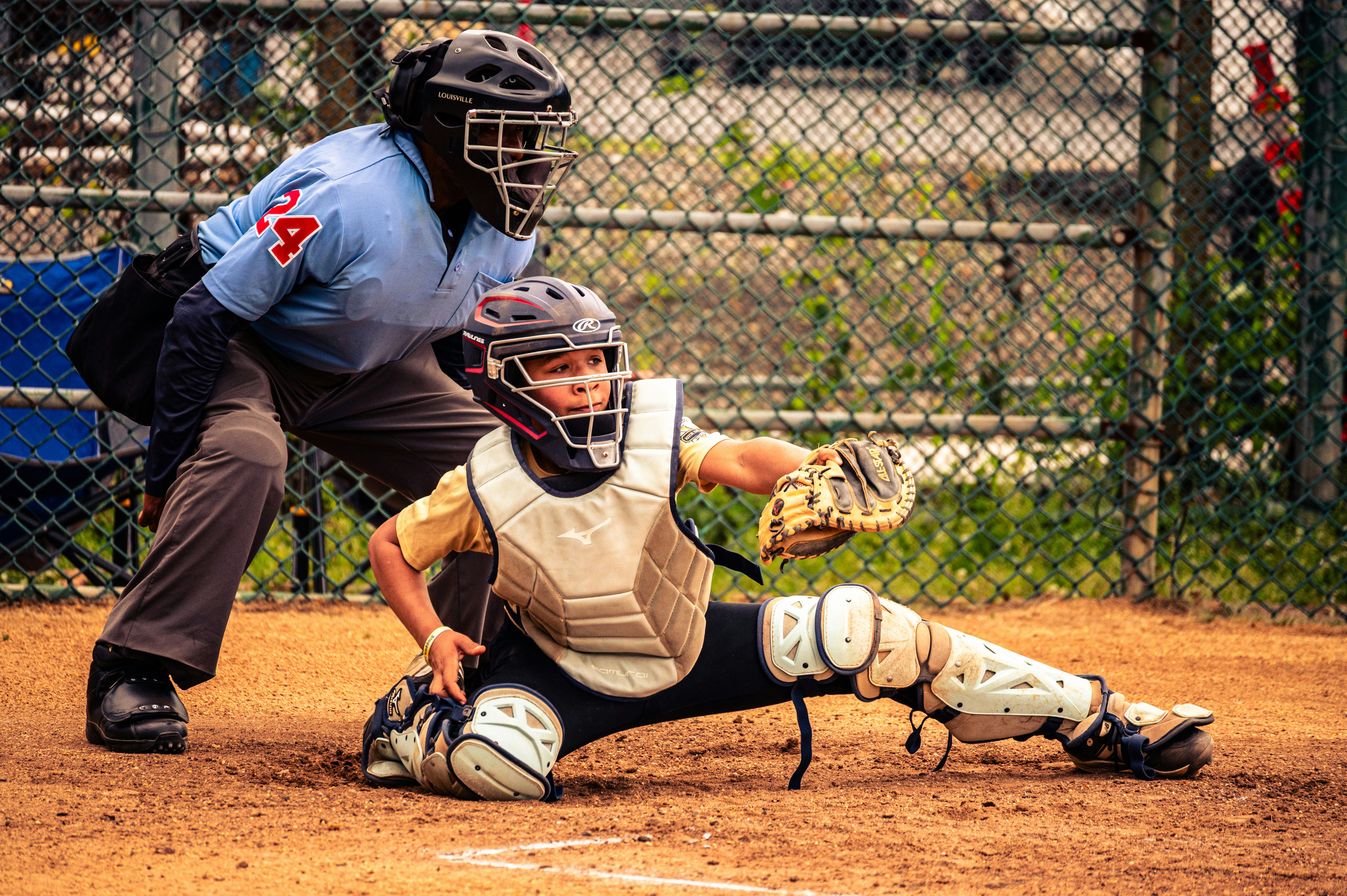 A baseball catcher in protective gear reaching for a ball behind an umpire