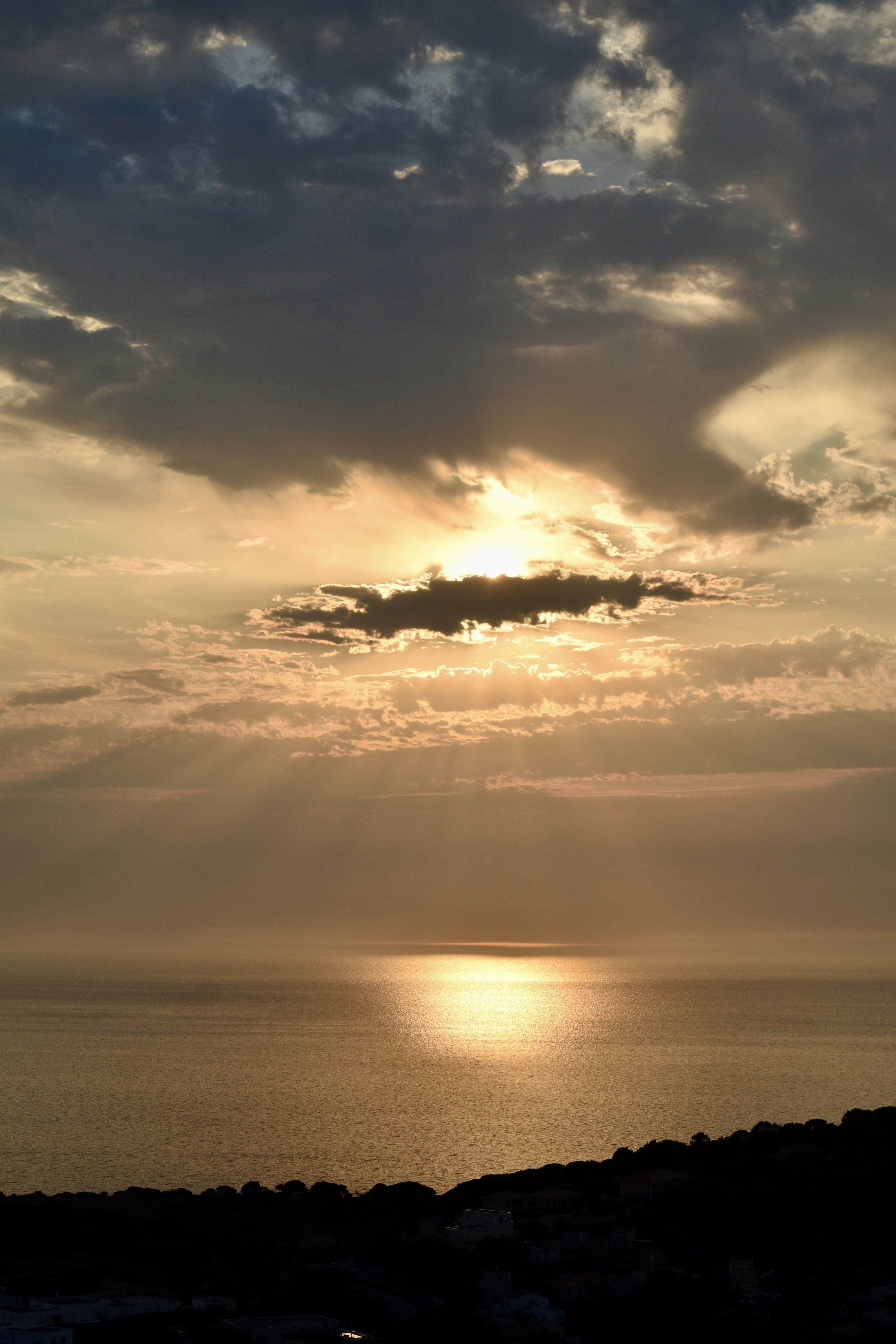 Golden light rays shining through clouds over a calm sea at low sun