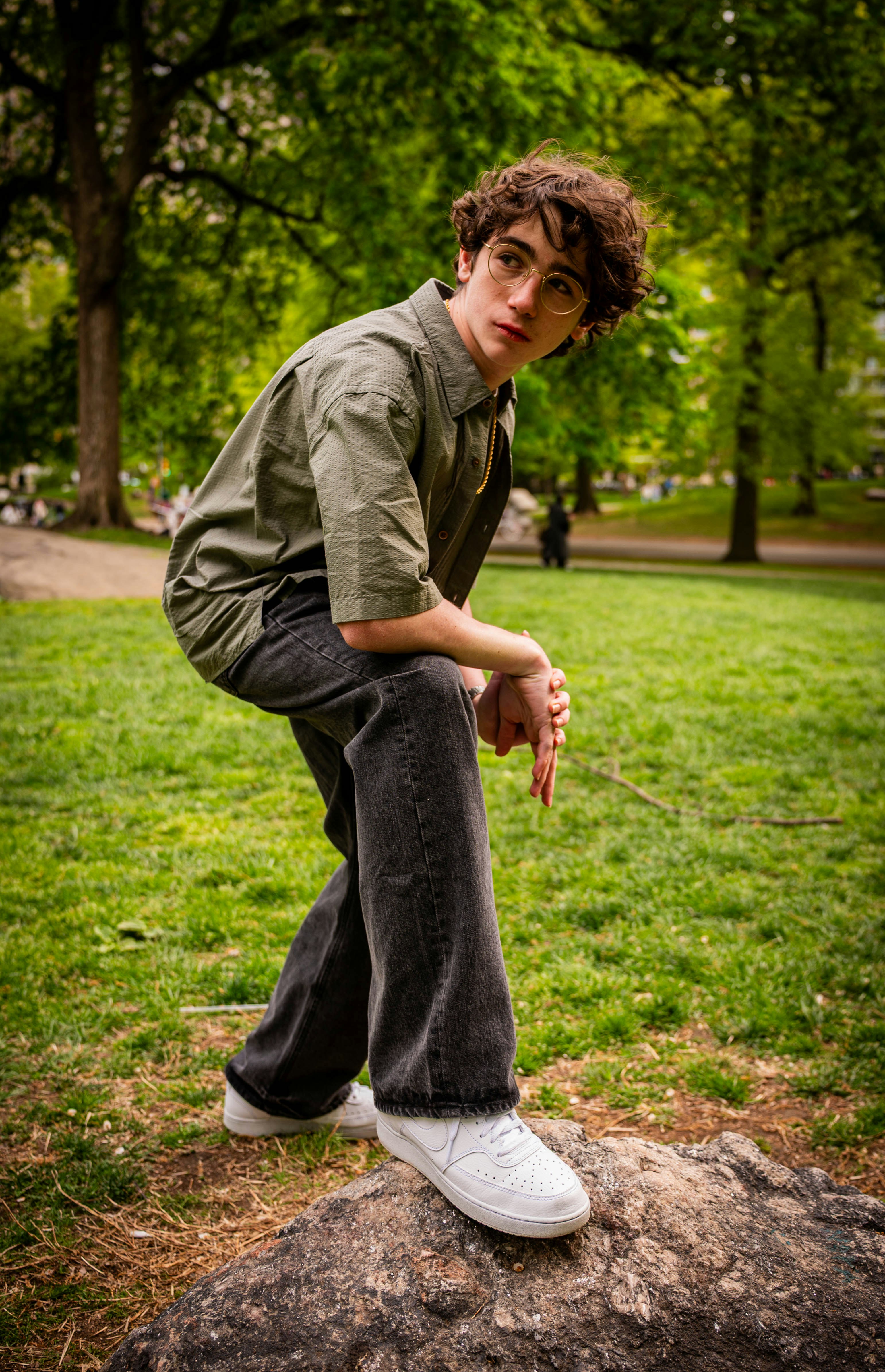 A person with curly hair and glasses in a green shirt on a rock