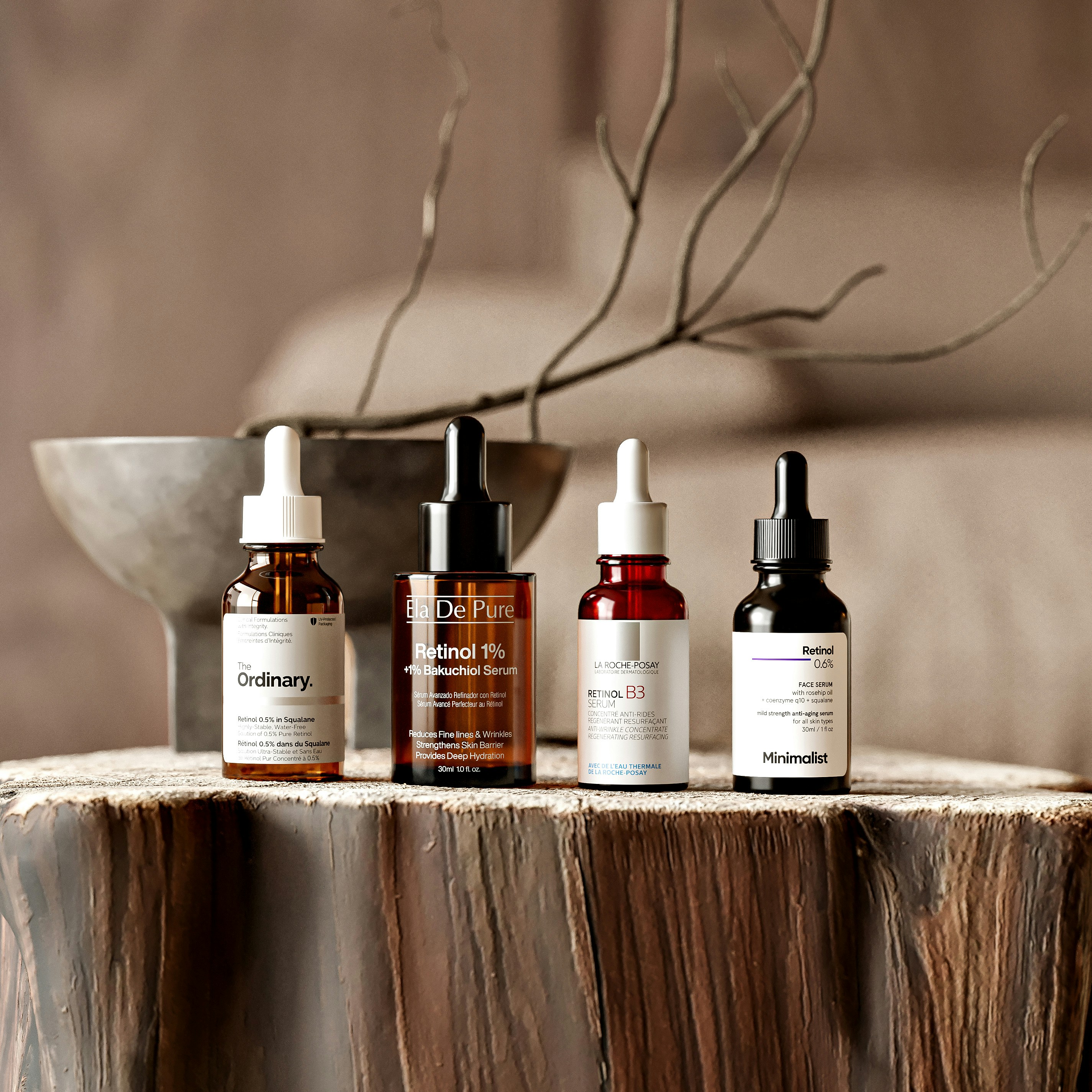 Four glass dropper bottles of facial serum on a rustic wooden stump