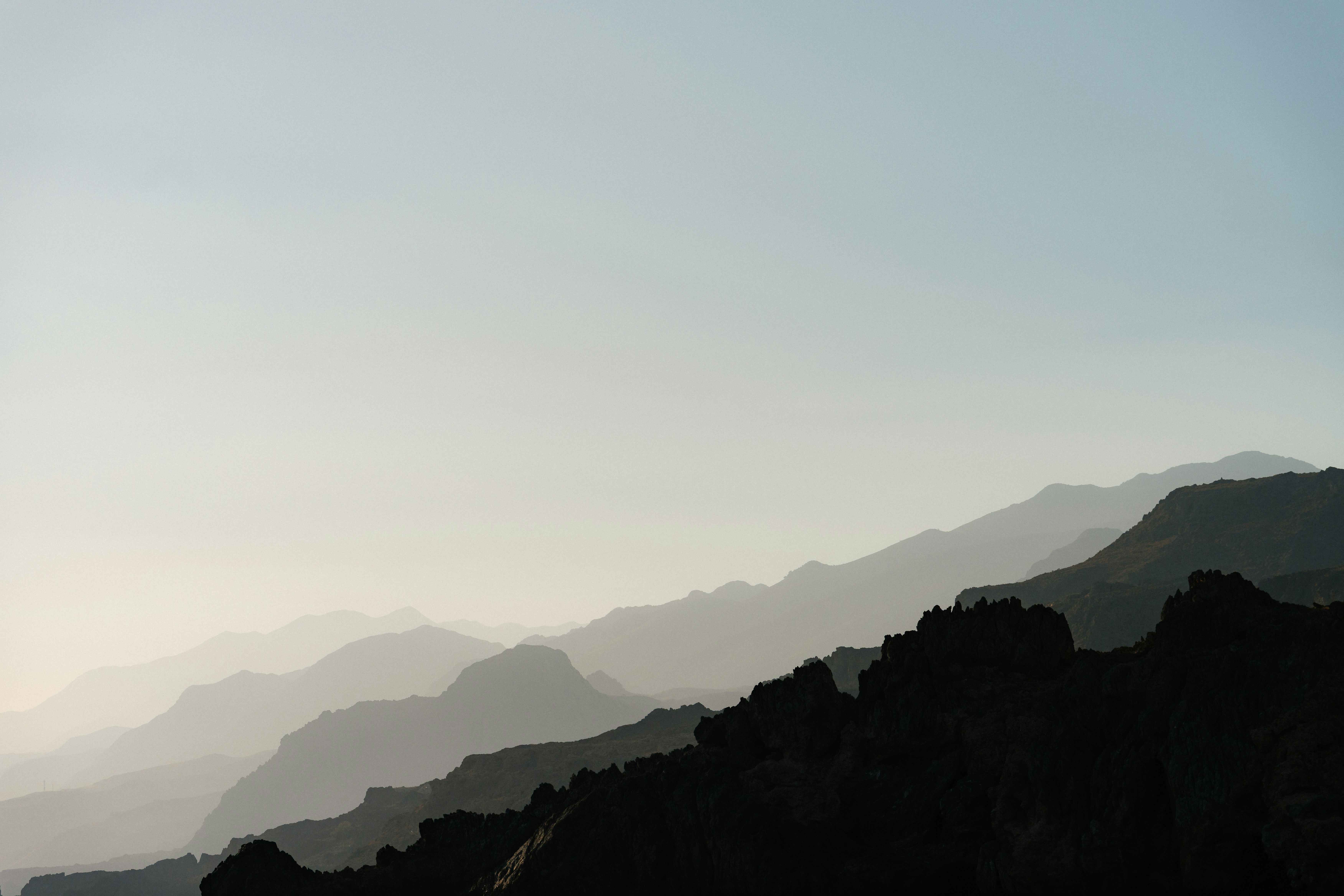 Layered mountain silhouettes fading into a pale hazy sky at low sun