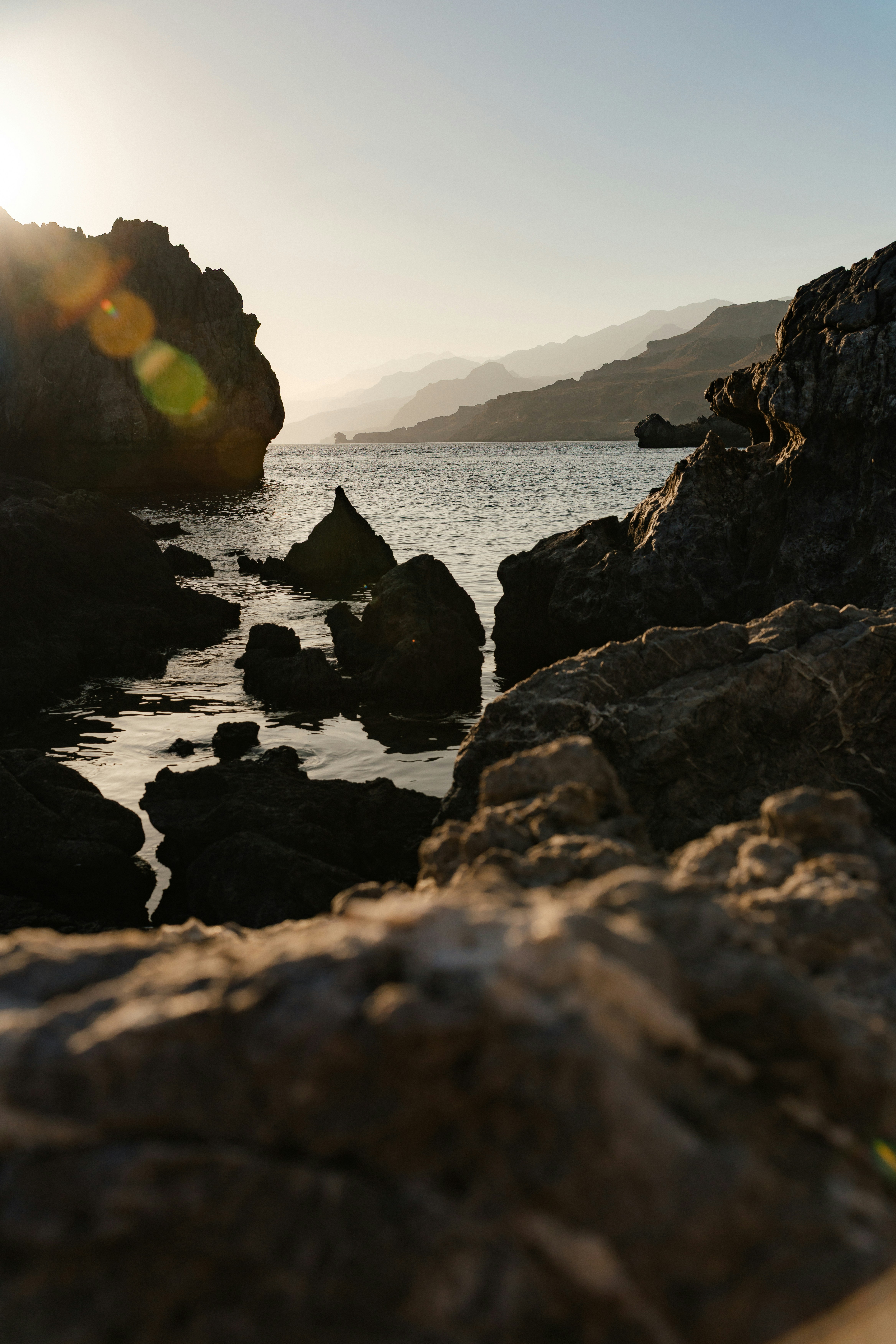 Jagged rocks in calm water under a low sun with distant hazy mountains