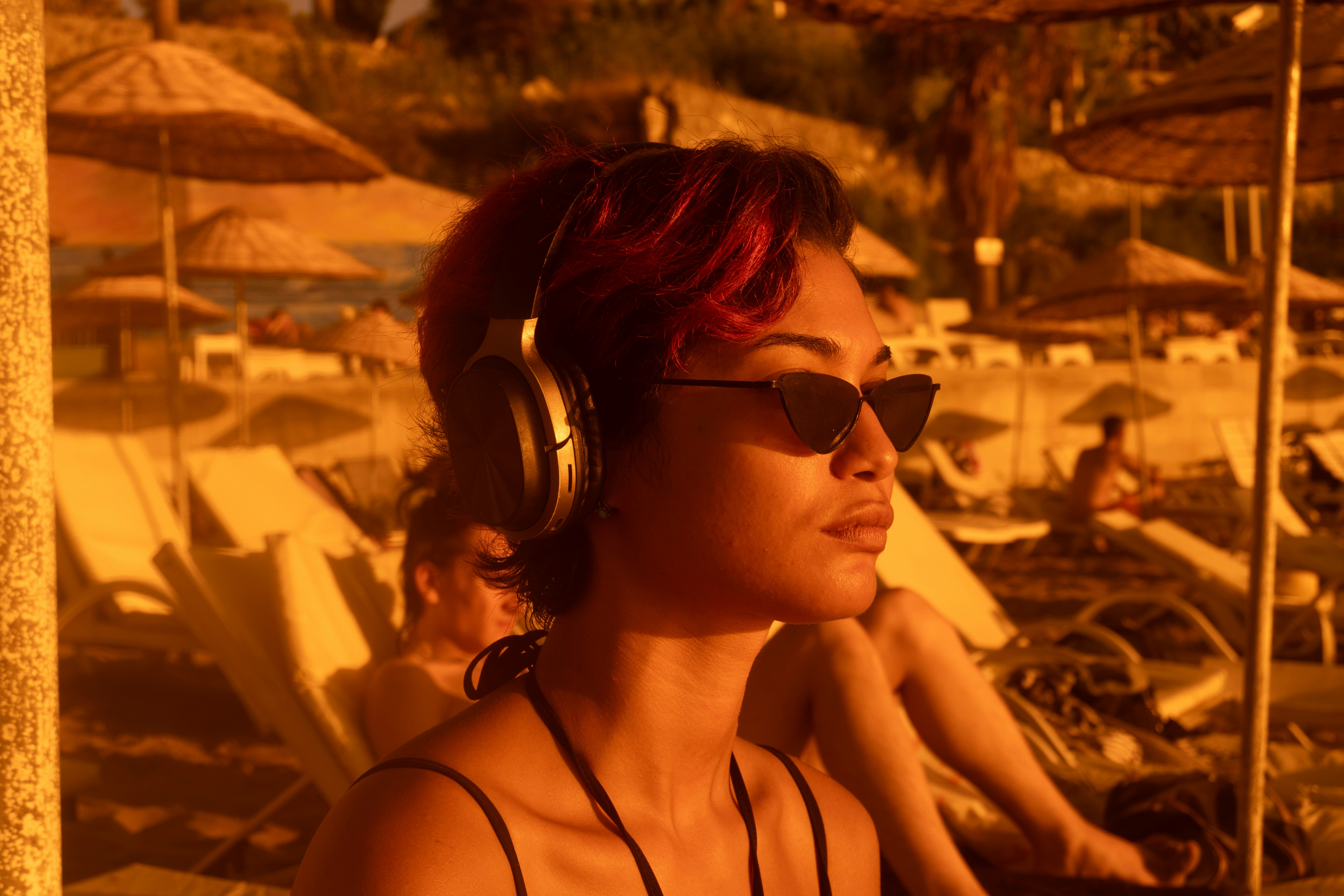 Una donna con capelli rossi che indossa cuffie e occhiali da sole su una spiaggia illuminata dal sole