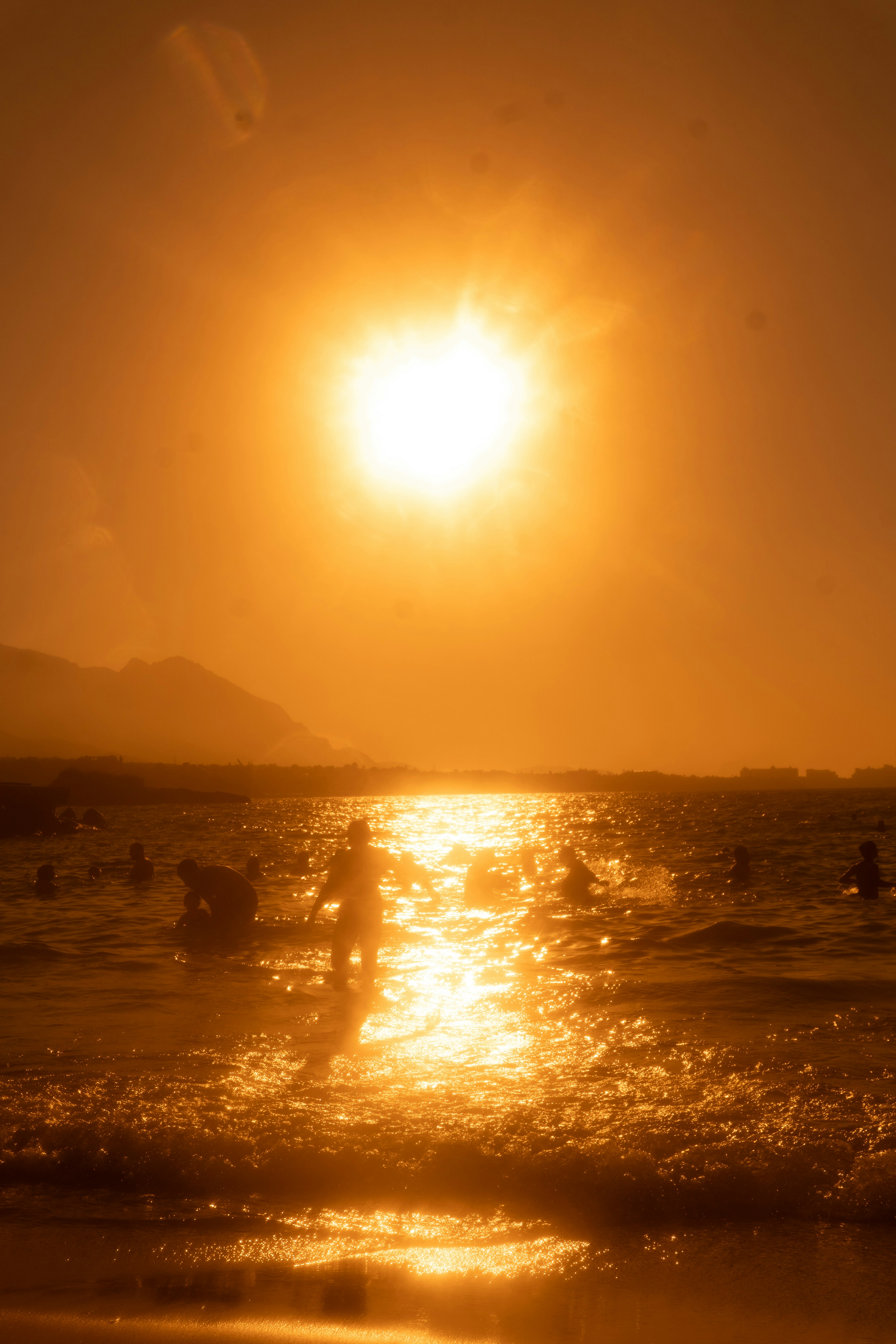 Silhouette di persone che nuotano nell'oceano sotto un sole basso e intenso