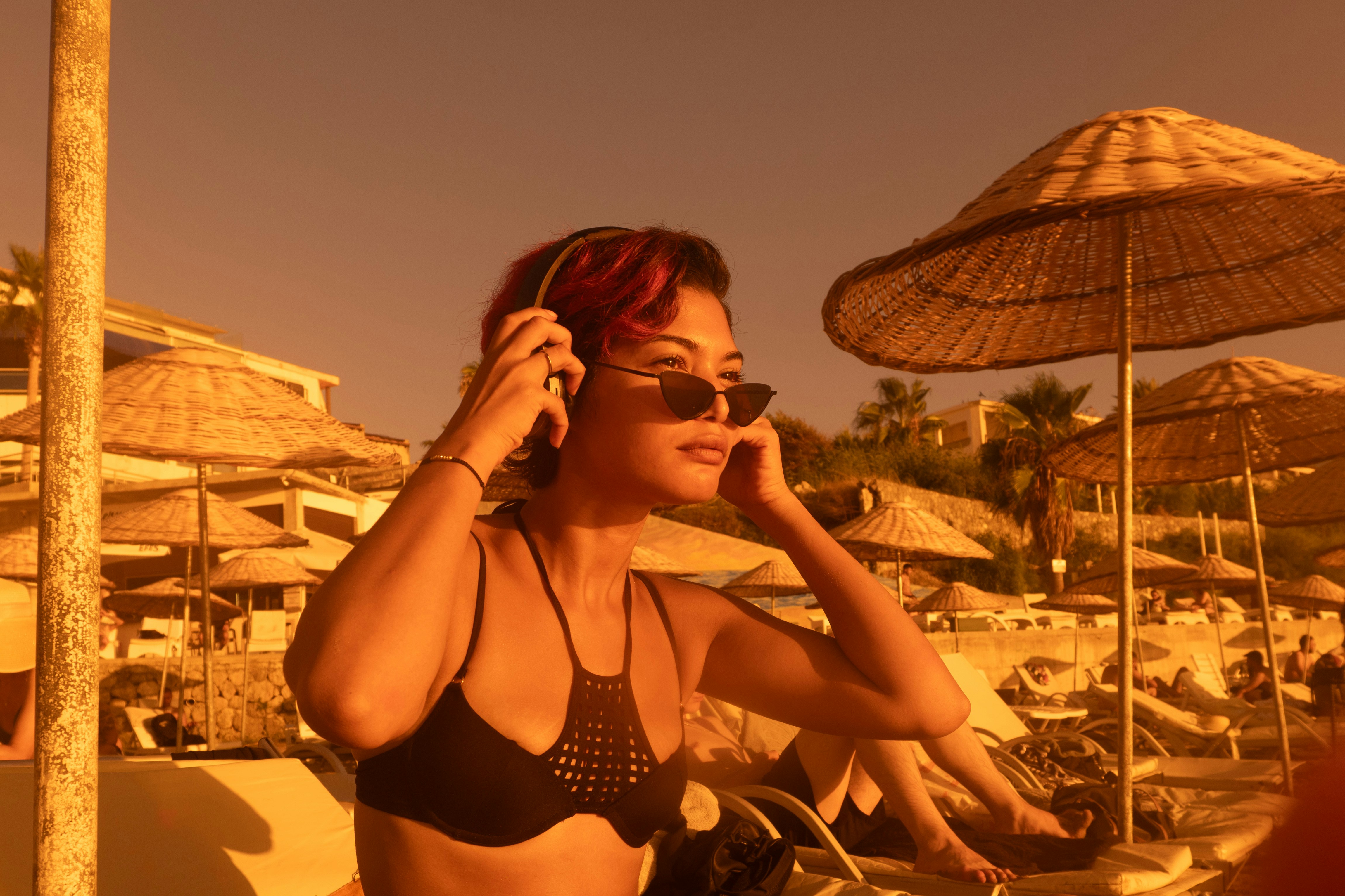Una donna con capelli rossi che indossa occhiali da sole e cuffie su una spiaggia illuminata dal sole