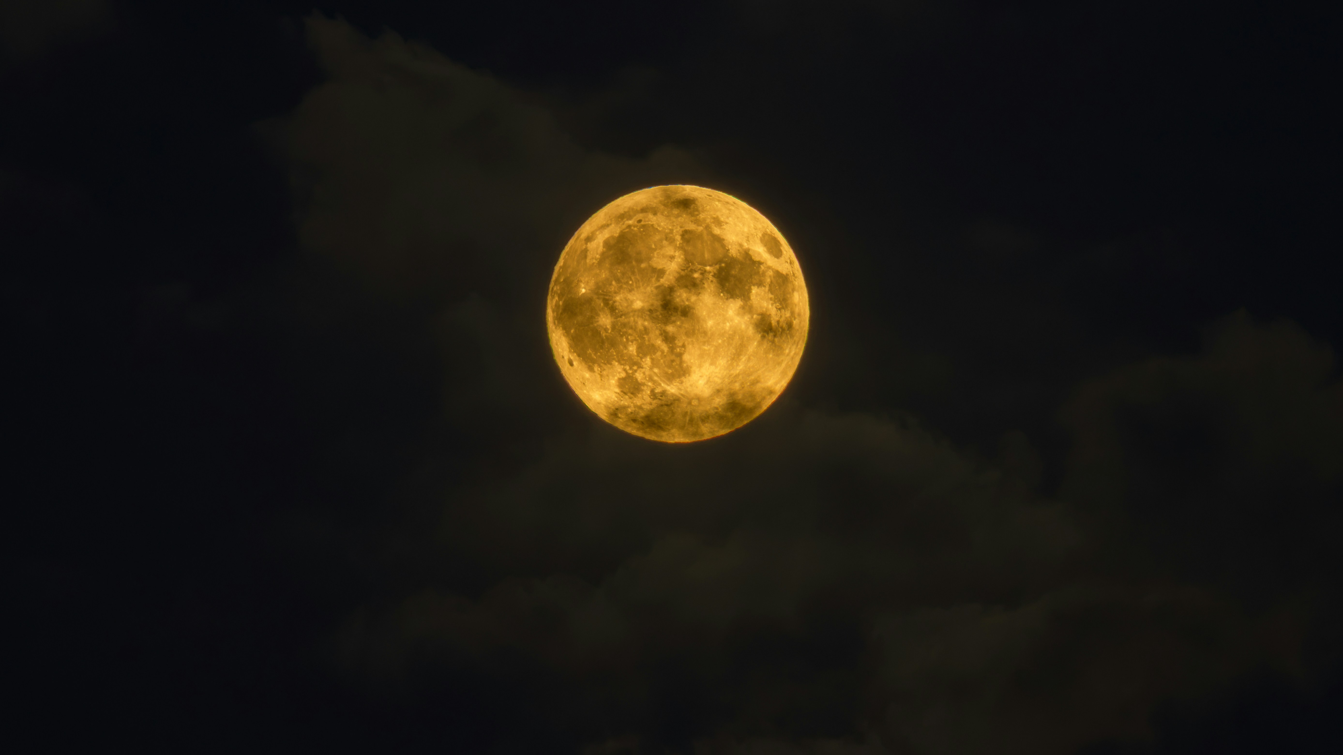 A golden full moon glowing against a dark night sky with soft clouds
